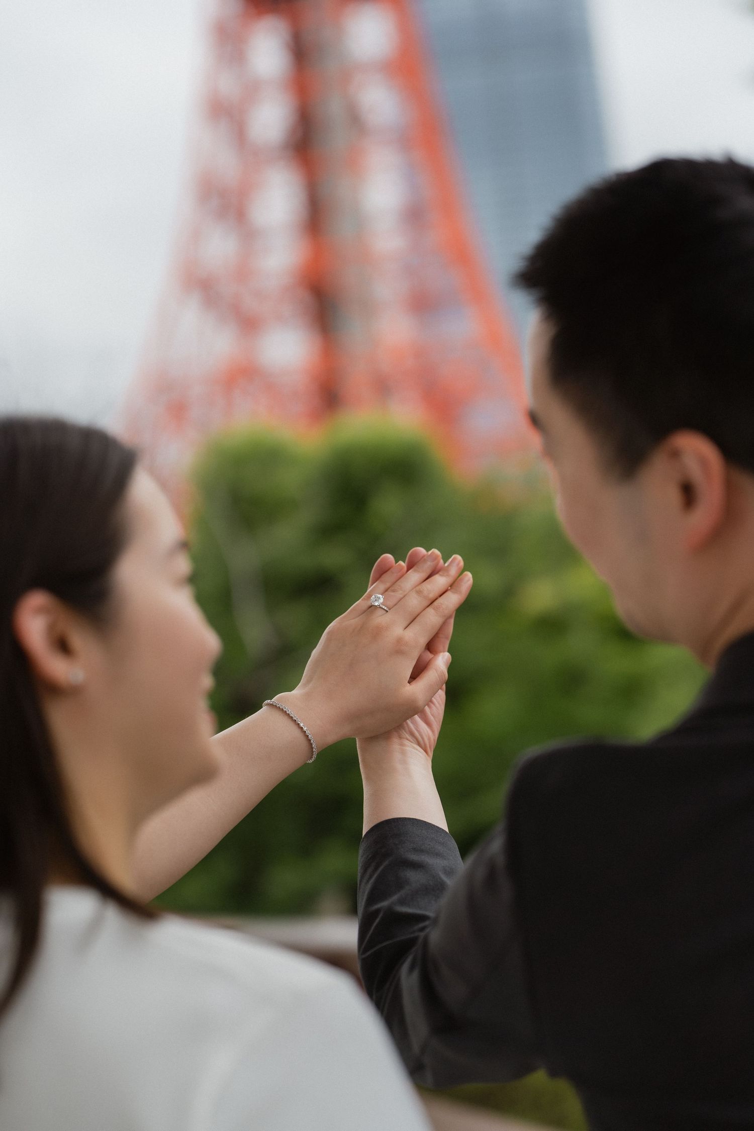 Couple holding hands showing engagement ring with Tokyo Tower in background.