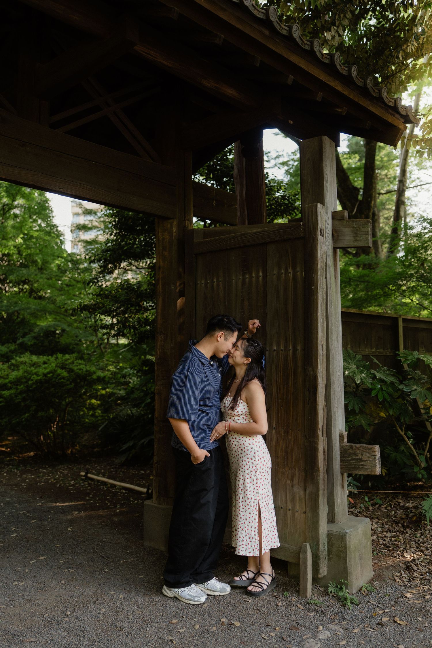 Couple sharing a kiss under a traditional wooden Japanese gate surrounded by green forest.