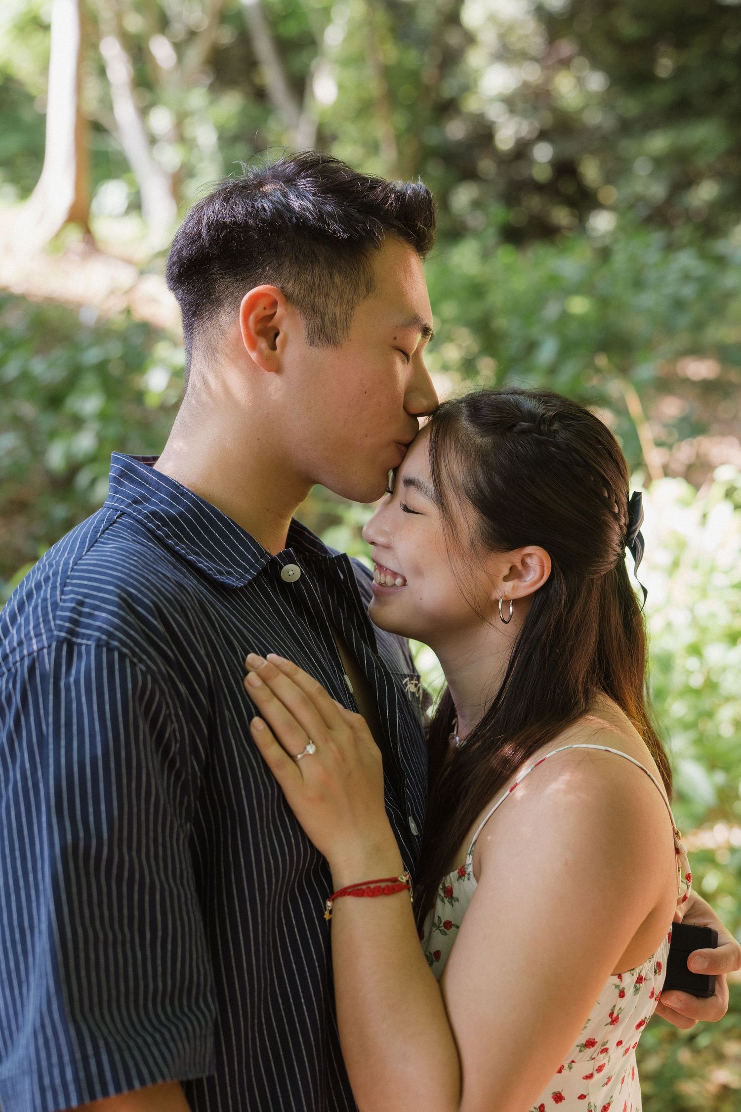 A couple shares a tender kiss outdoors, surrounded by lush green foliage in a romantic garden setting.