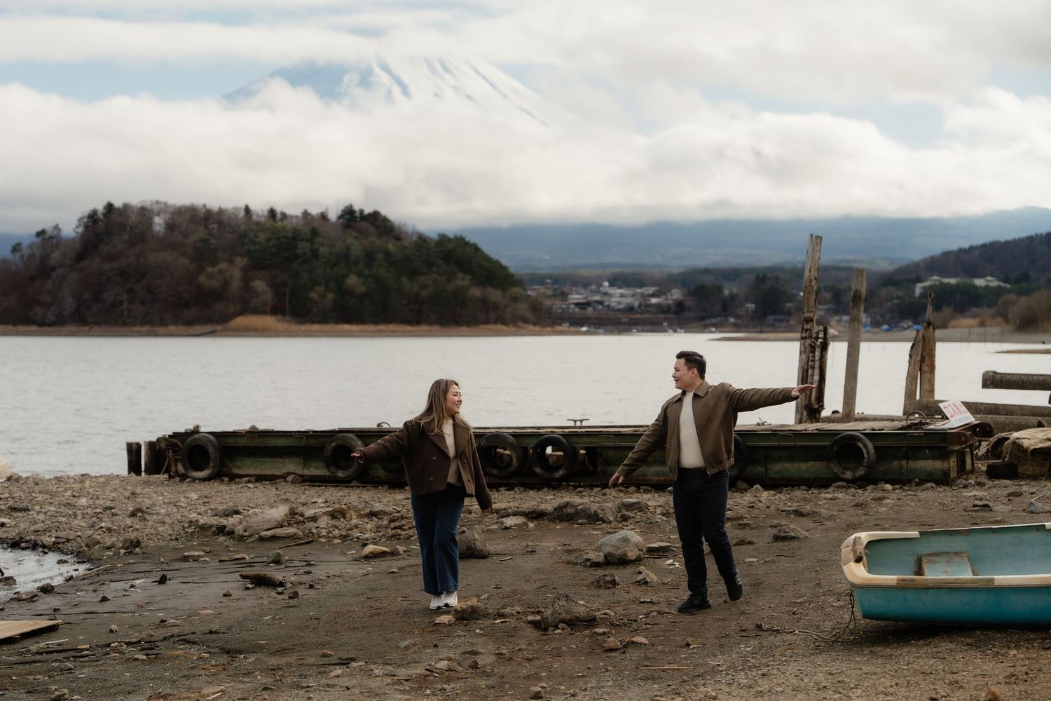Couple walking on rocky shore of Lake Kawaguchi with snow-capped Mount Fuji in background, Japan.