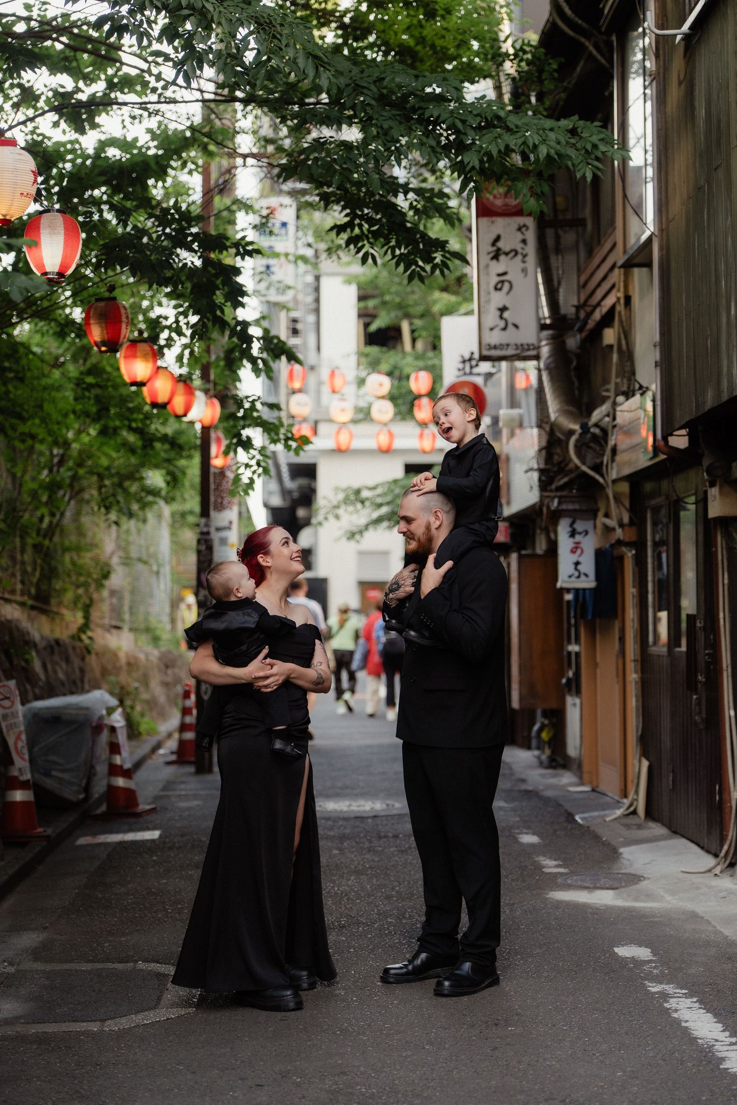 Family in black attire poses on a charming Japanese alley with red lanterns and traditional shopfronts.