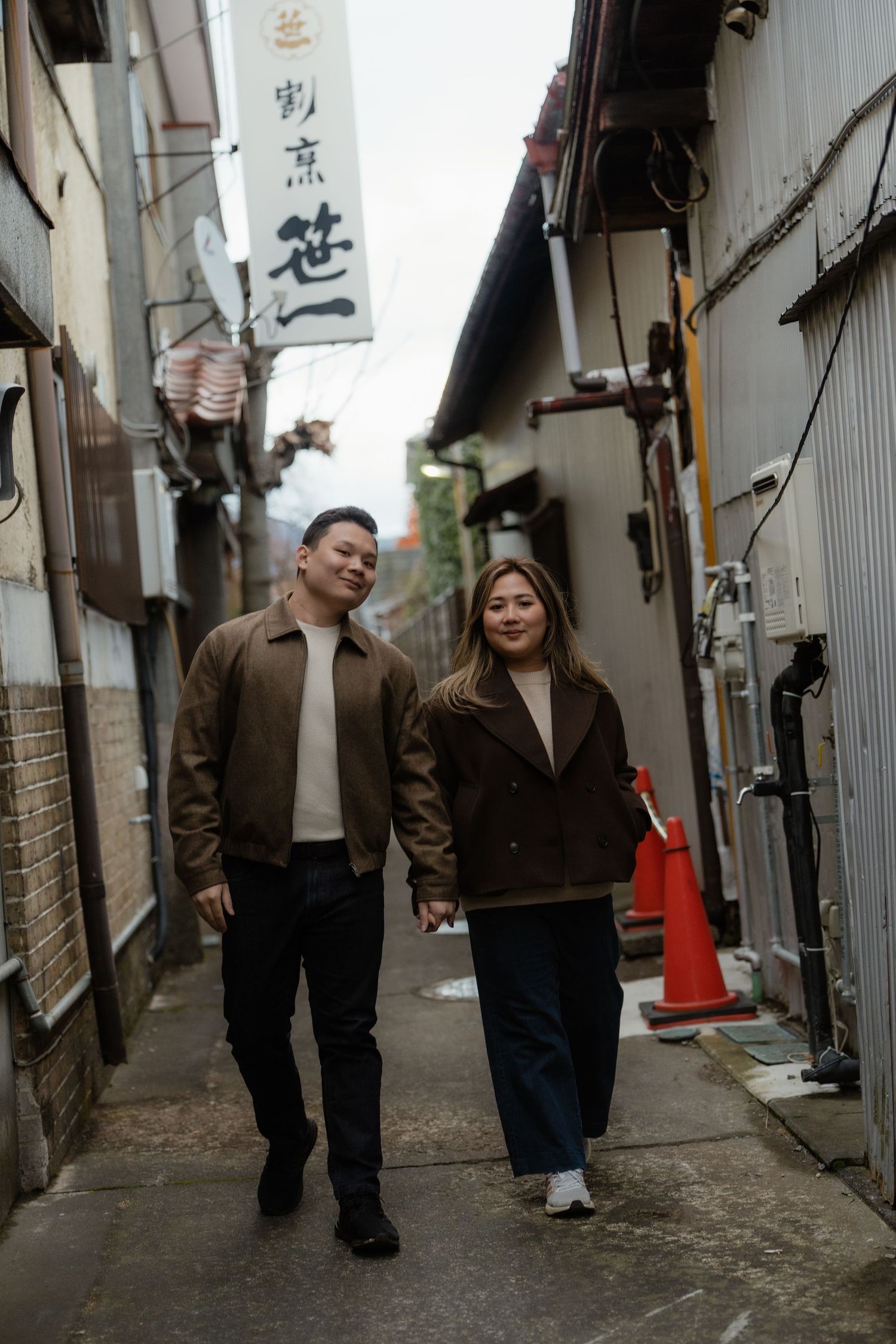 Couple holding hands walking through a narrow Japanese alley with traditional buildings and signage.