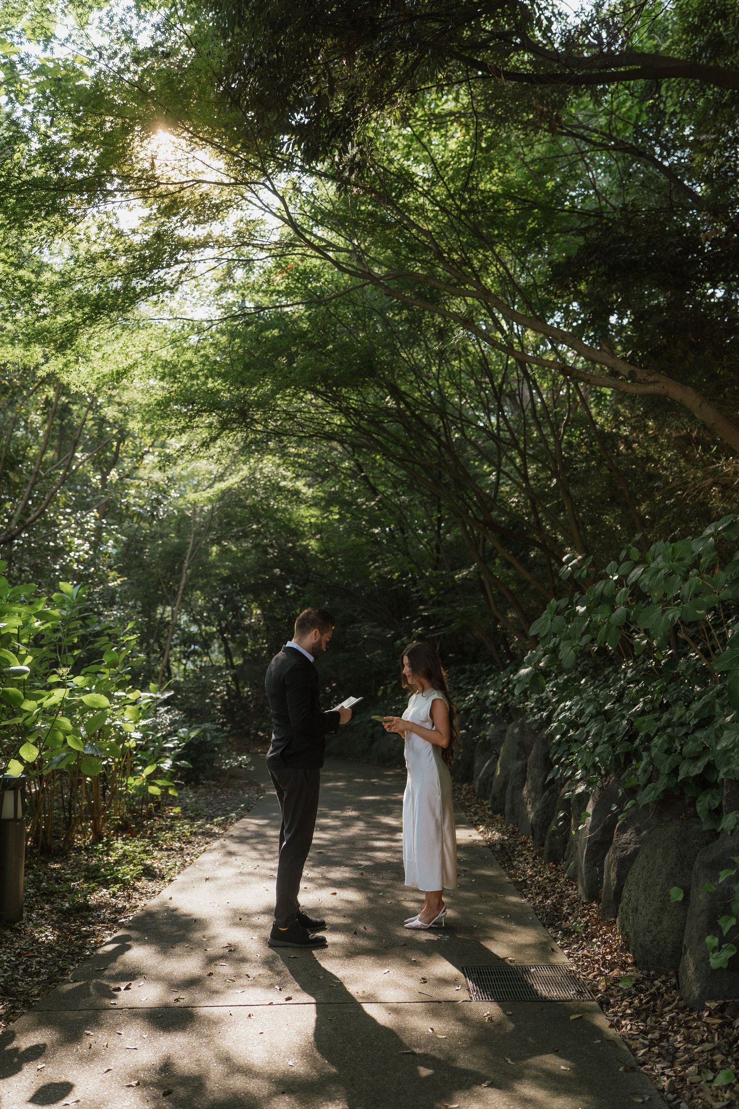 Couple exchanging vows on a lush garden path surrounded by green trees during an intimate outdoor wedding ceremony.