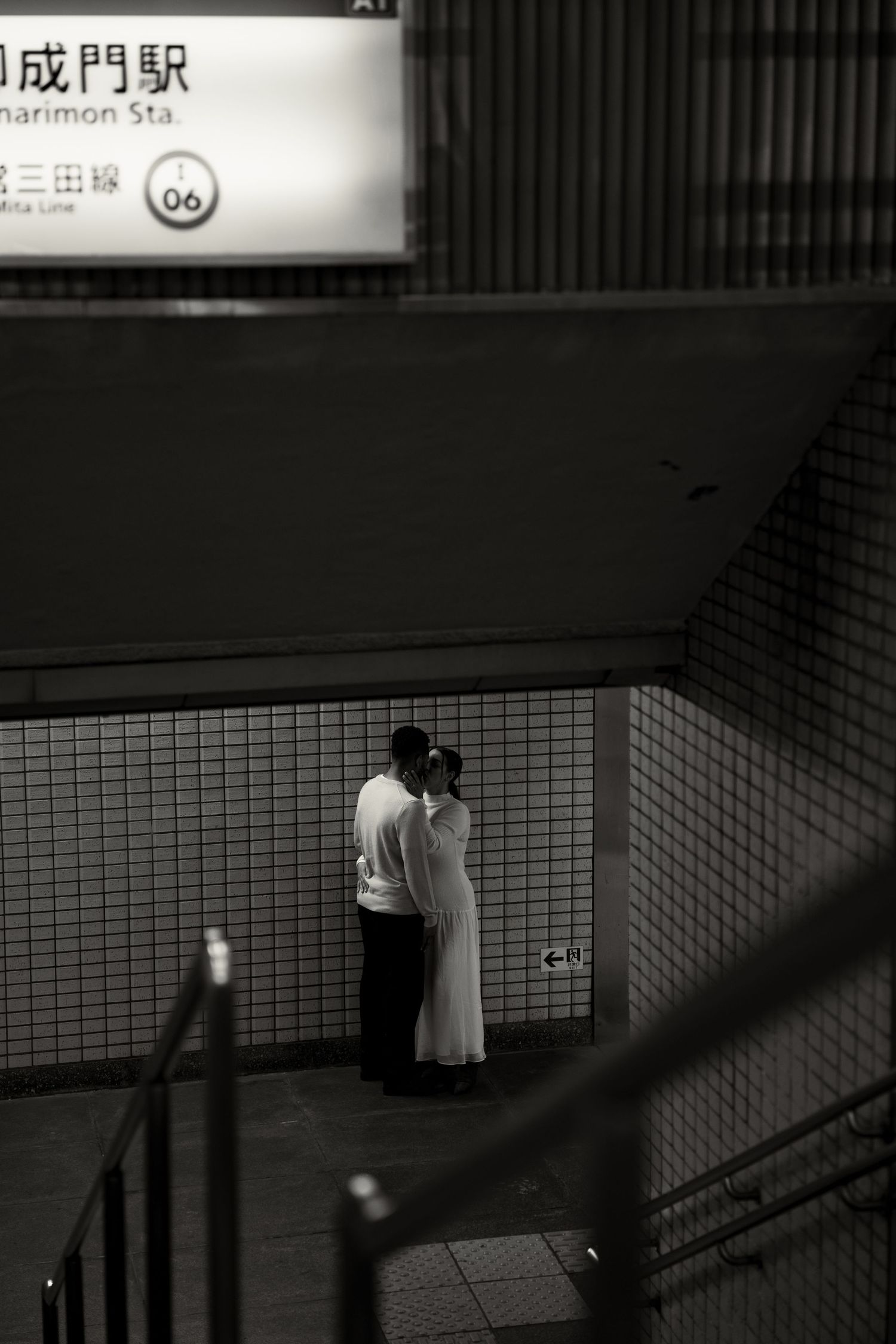 Black and white photo of a couple embracing near Tameike-Sanno subway station entrance in Tokyo, Japan at night.
