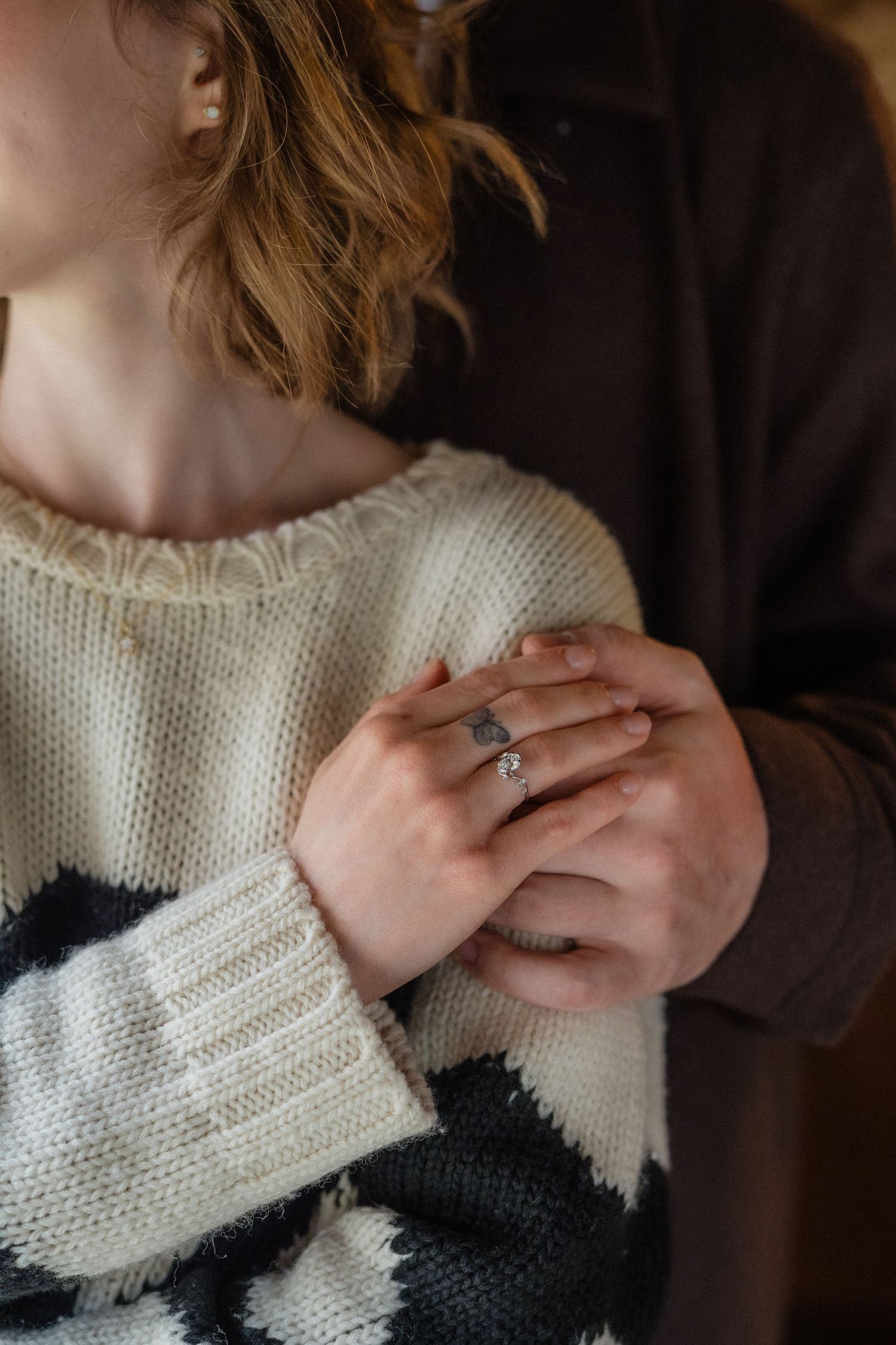 Close-up of couple holding hands, woman wearing diamond engagement ring, cozy knit sweater, romantic moment.