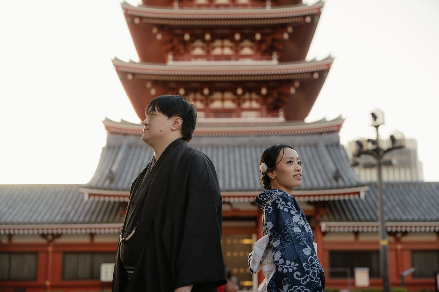 Couple in traditional Japanese kimono posing back-to-back at Senso-ji temple pagoda in Tokyo, Japan.