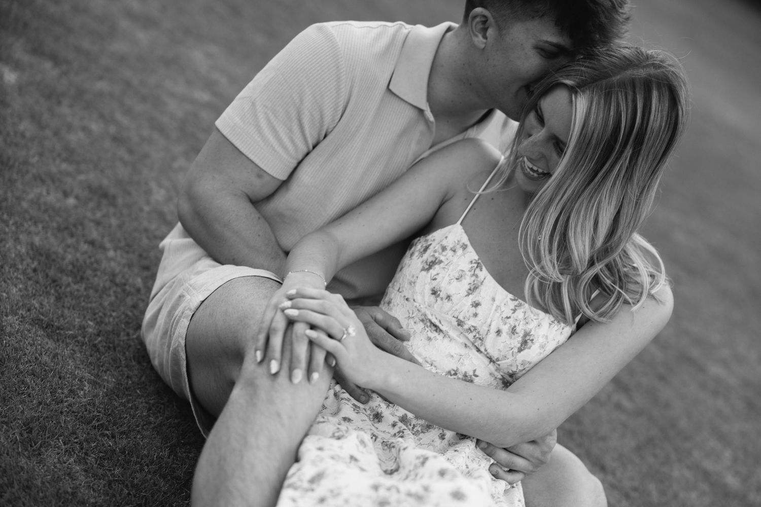 Black and white photo of a couple sitting closely together on grass, smiling.
