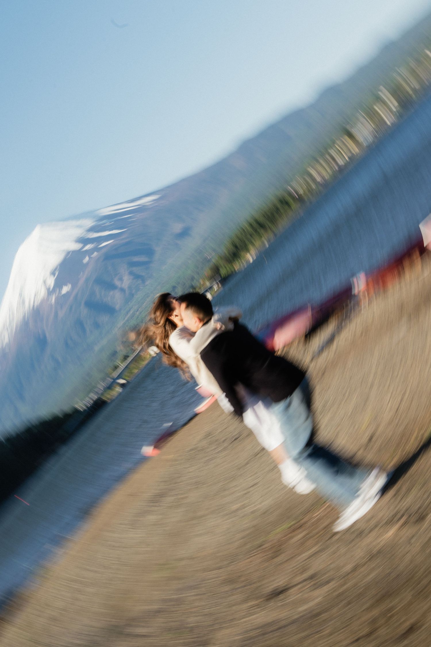 Blurred zoom effect photo of a couple kissing near a mountain lake on their wedding day.