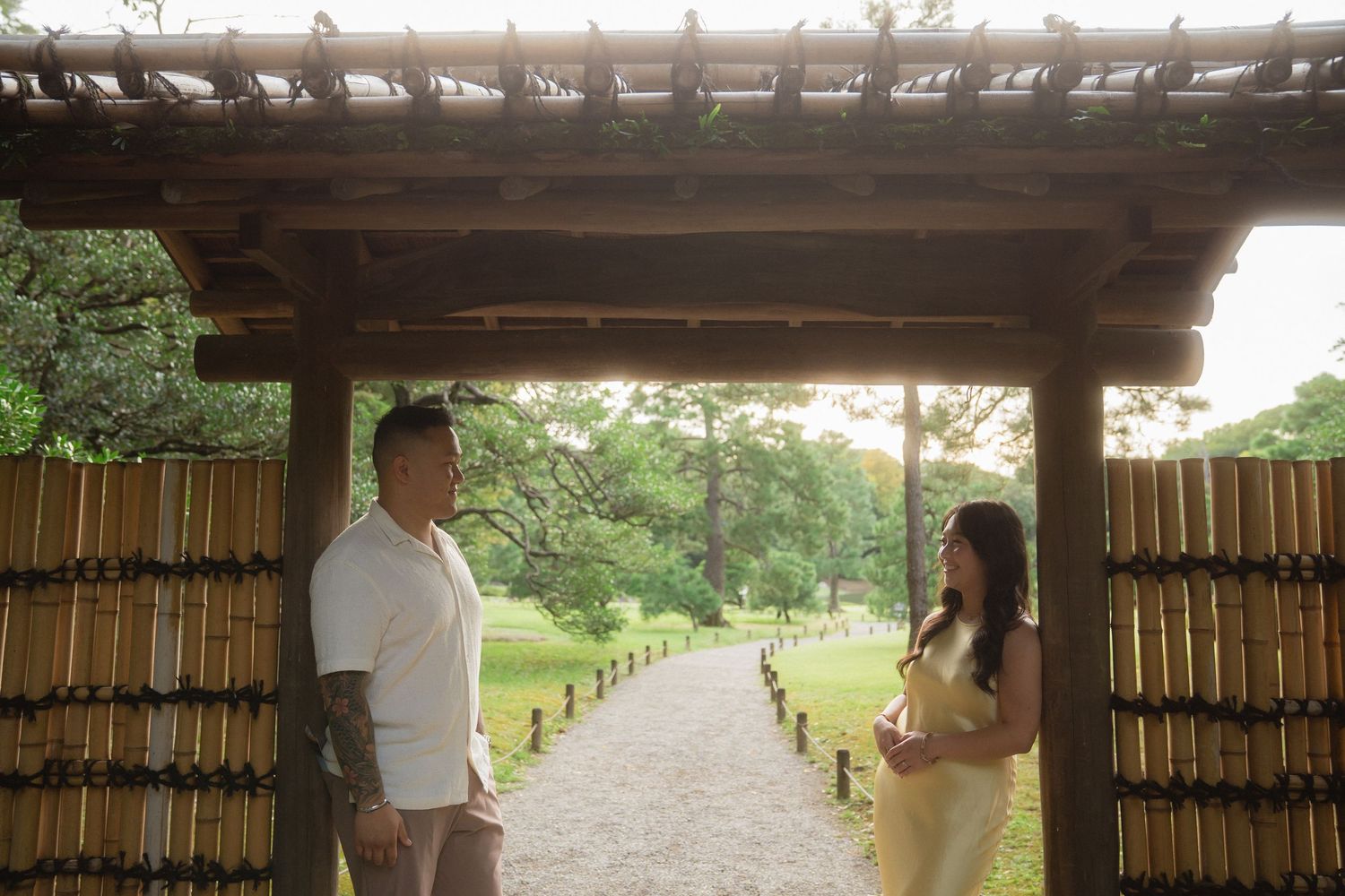 Couple standing under a bamboo gate in a Japanese garden with a stone pathway and lush greenery.