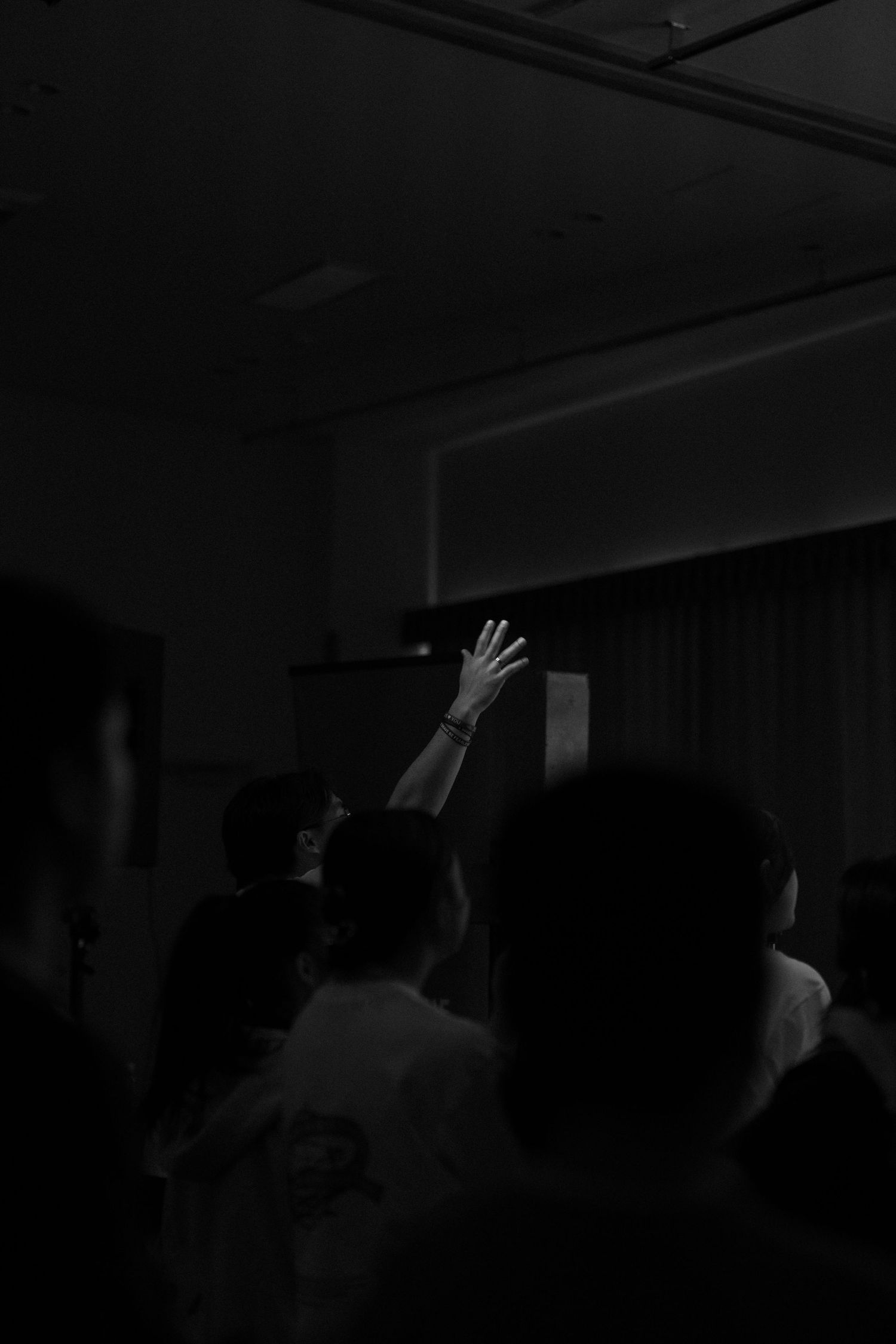 Black and white photo of a crowd with one person raising their hand up at an indoor event or concert.