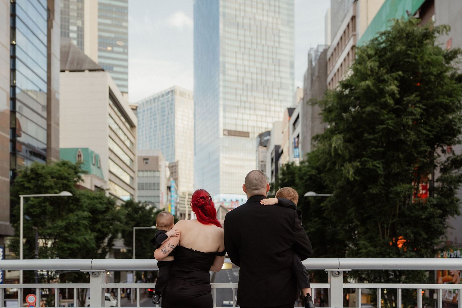 Three people stand together on a city bridge, gazing at towering skyscrapers in a bustling urban landscape.