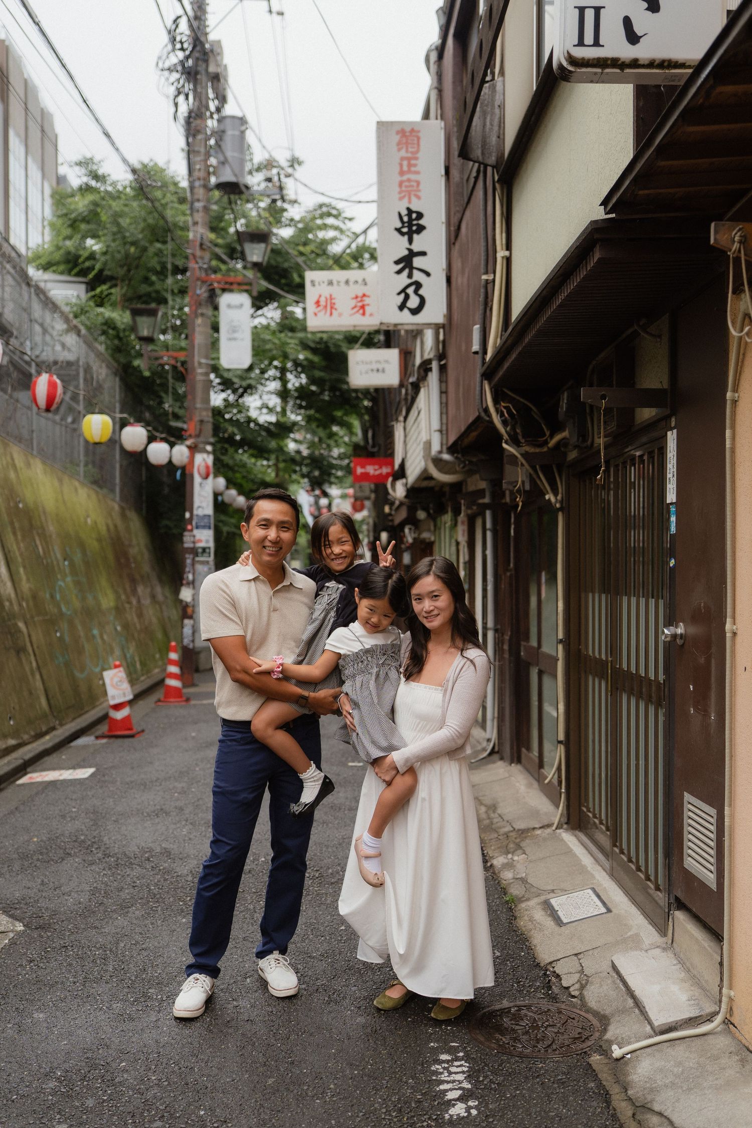 Family of four posing on a charming narrow street in Japan, with traditional shop signs and lanterns in the background.