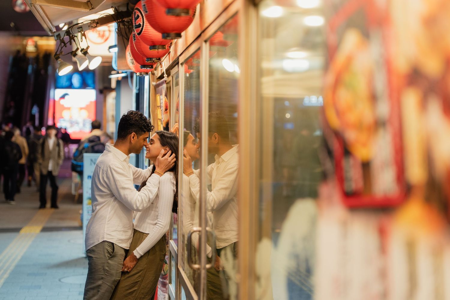 Couple sharing a romantic moment outside a vibrant Asian street restaurant at night.