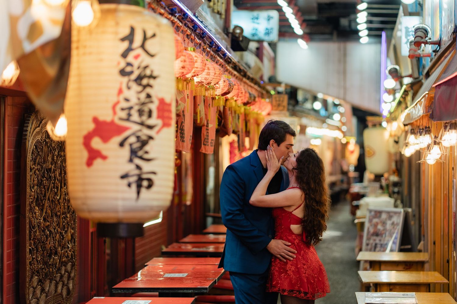 Couple kissing romantically in a vibrant Japanese market alley with glowing red lanterns and kanji signs.