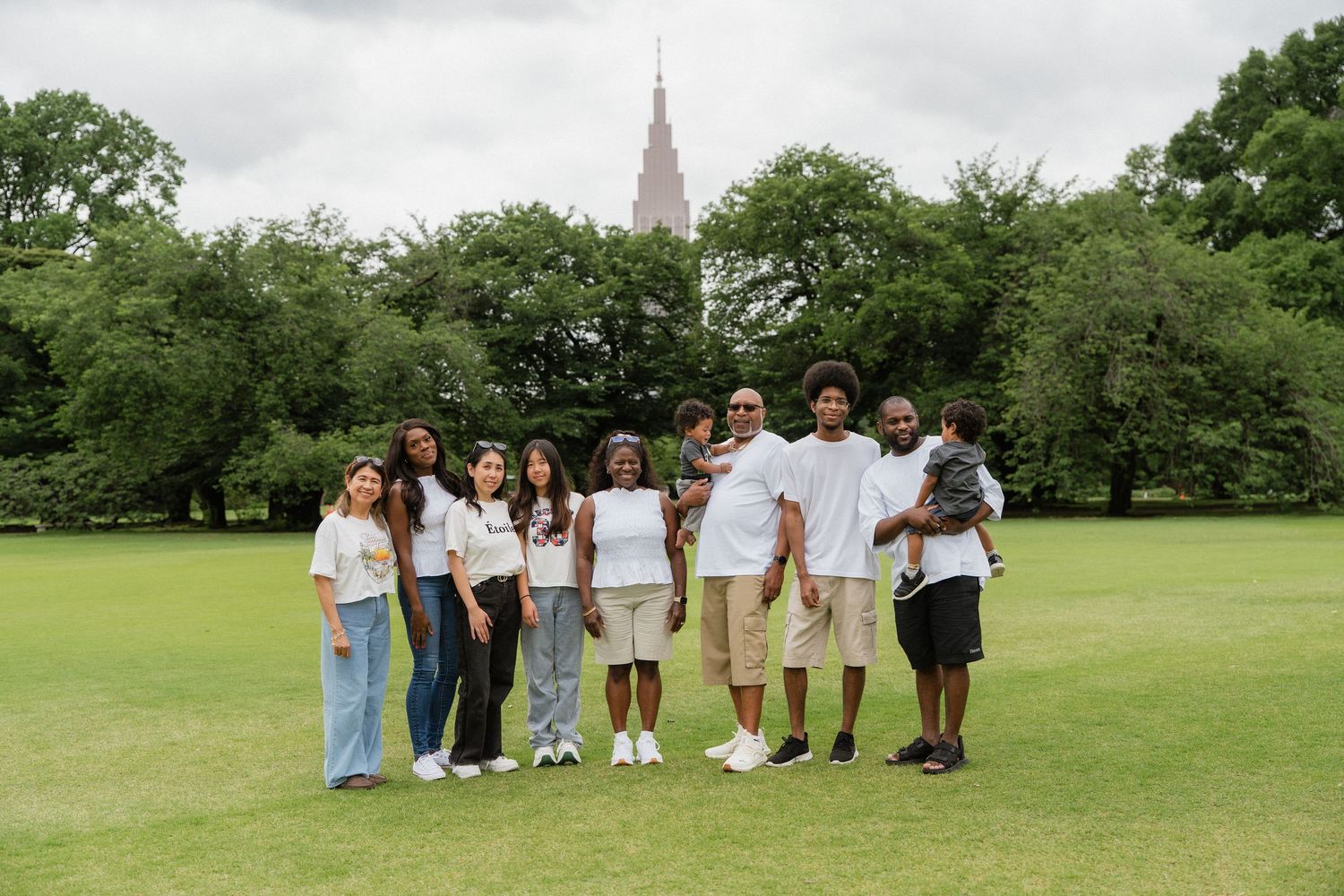 A diverse family group poses on a green lawn with trees and a church spire in the background.