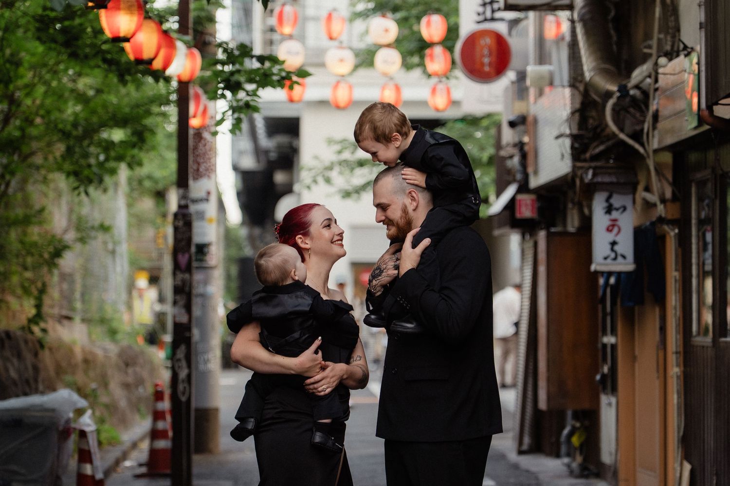 Happy family with two young children posing in a vibrant Japanese alley with red paper lanterns.