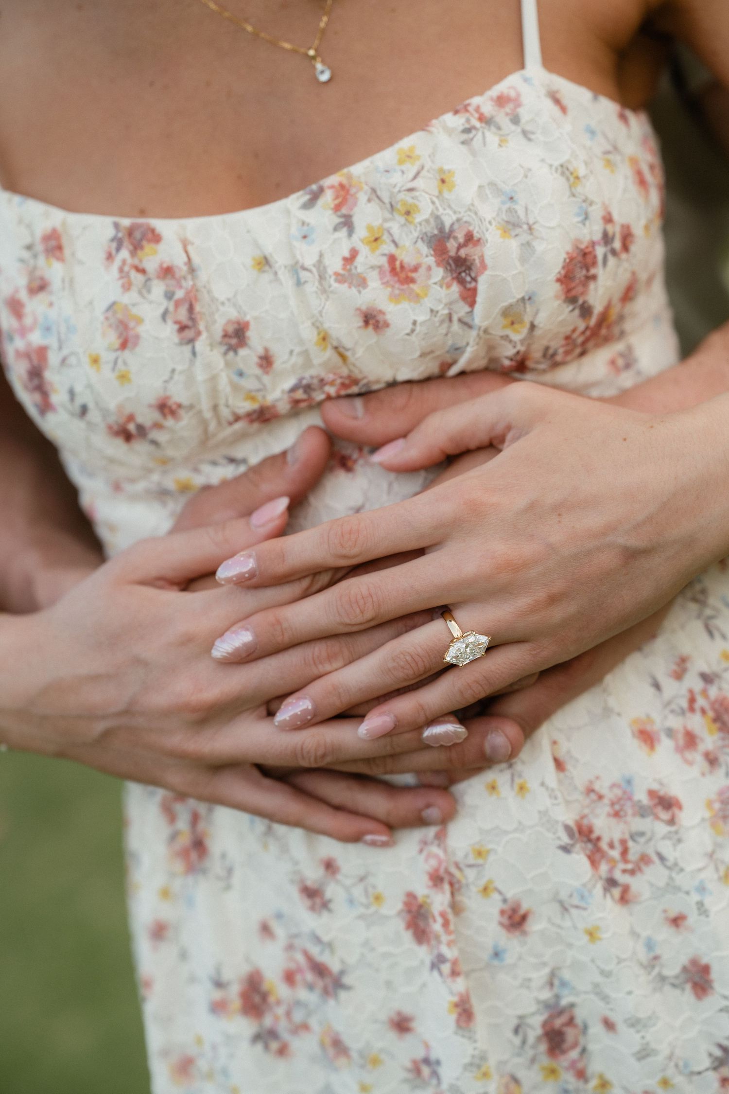 Close-up of hands with engagement ring on floral dress, couple embracing tenderly.