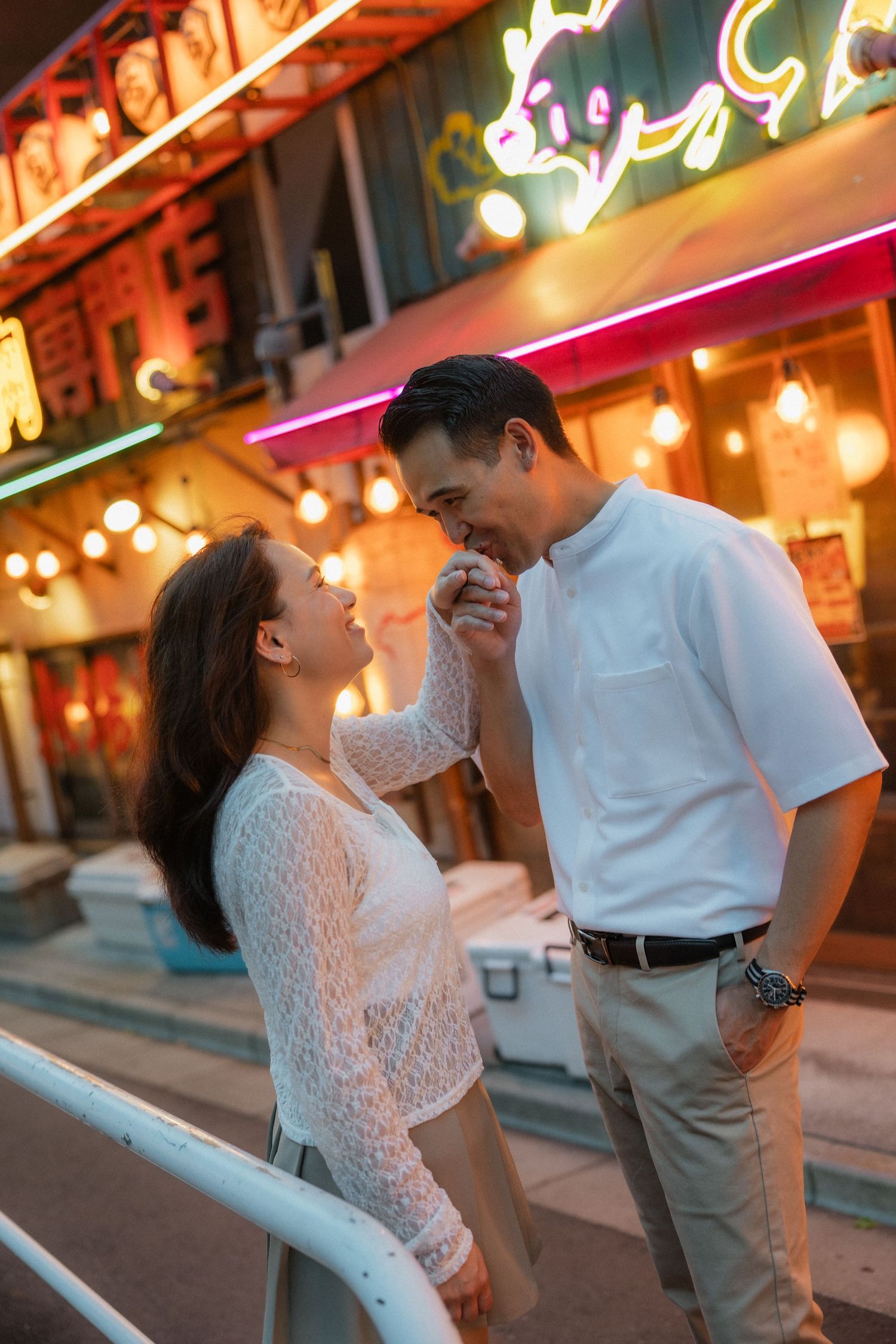 Romantic couple sharing a tender moment outside a neon-lit restaurant at night.