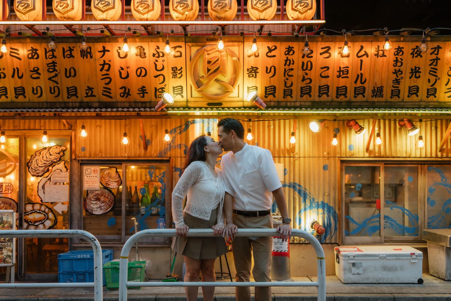 Couple sharing a romantic moment kissing in front of a glowing Japanese lantern restaurant facade at night.