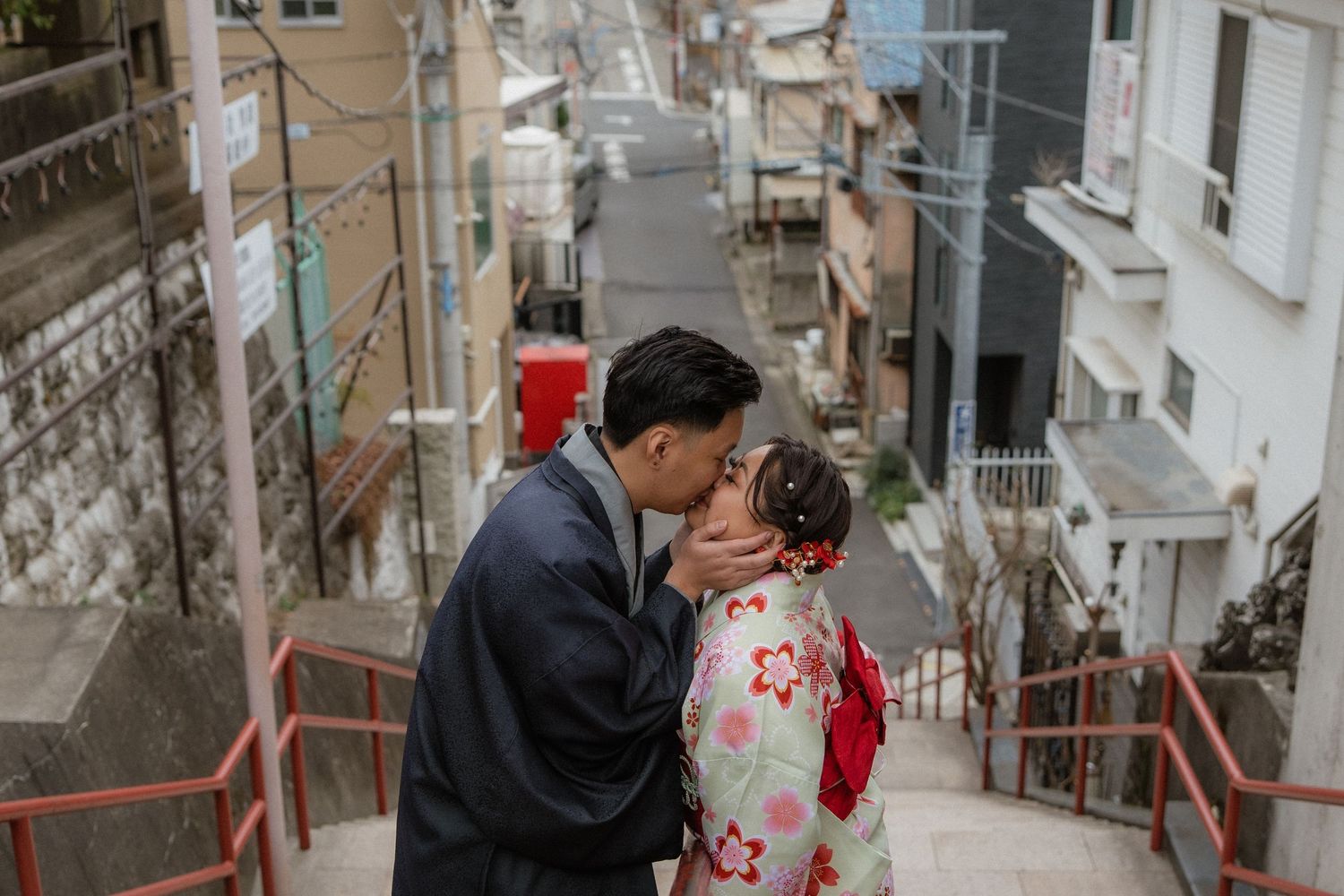 Couple in traditional Japanese kimono sharing a kiss on scenic stairway street in Japan.
