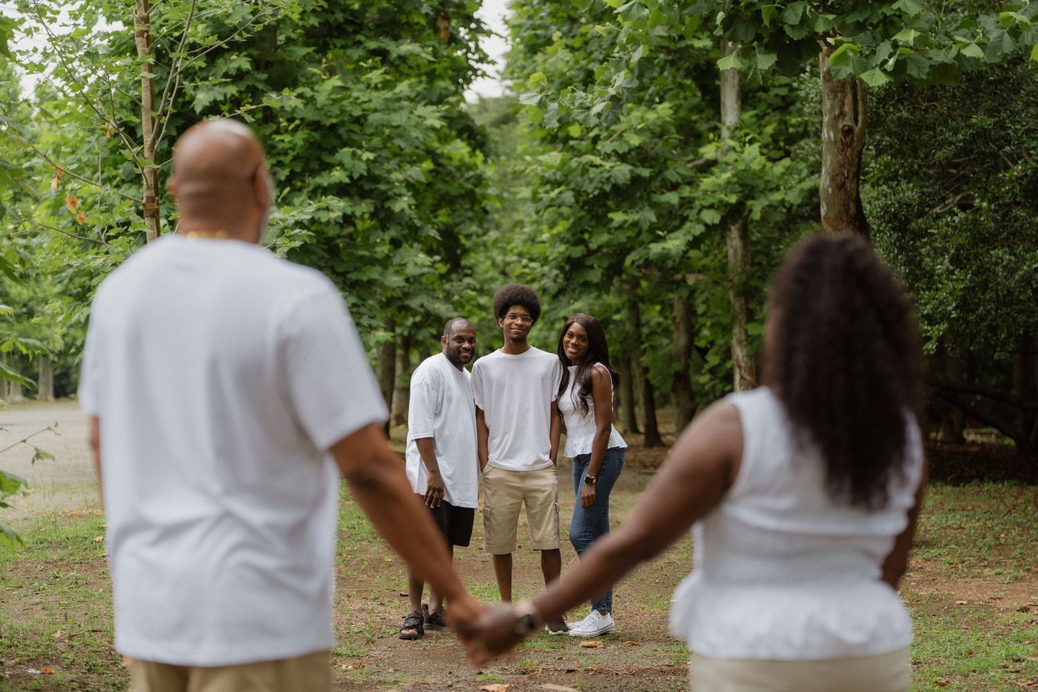 Family holding hands in a lush green forest park, wearing matching white outfits during an outdoor photo session.