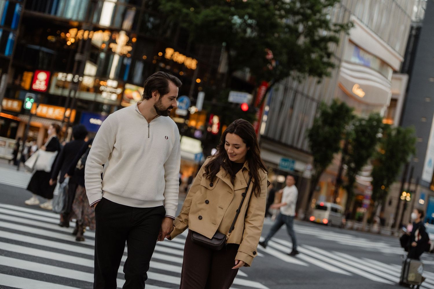 Couple holding hands while crossing a busy urban street intersection in Tokyo, Japan at dusk.