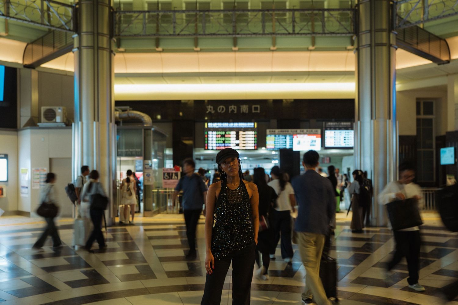Woman standing in a busy Japanese train station concourse with commuters walking in the background.