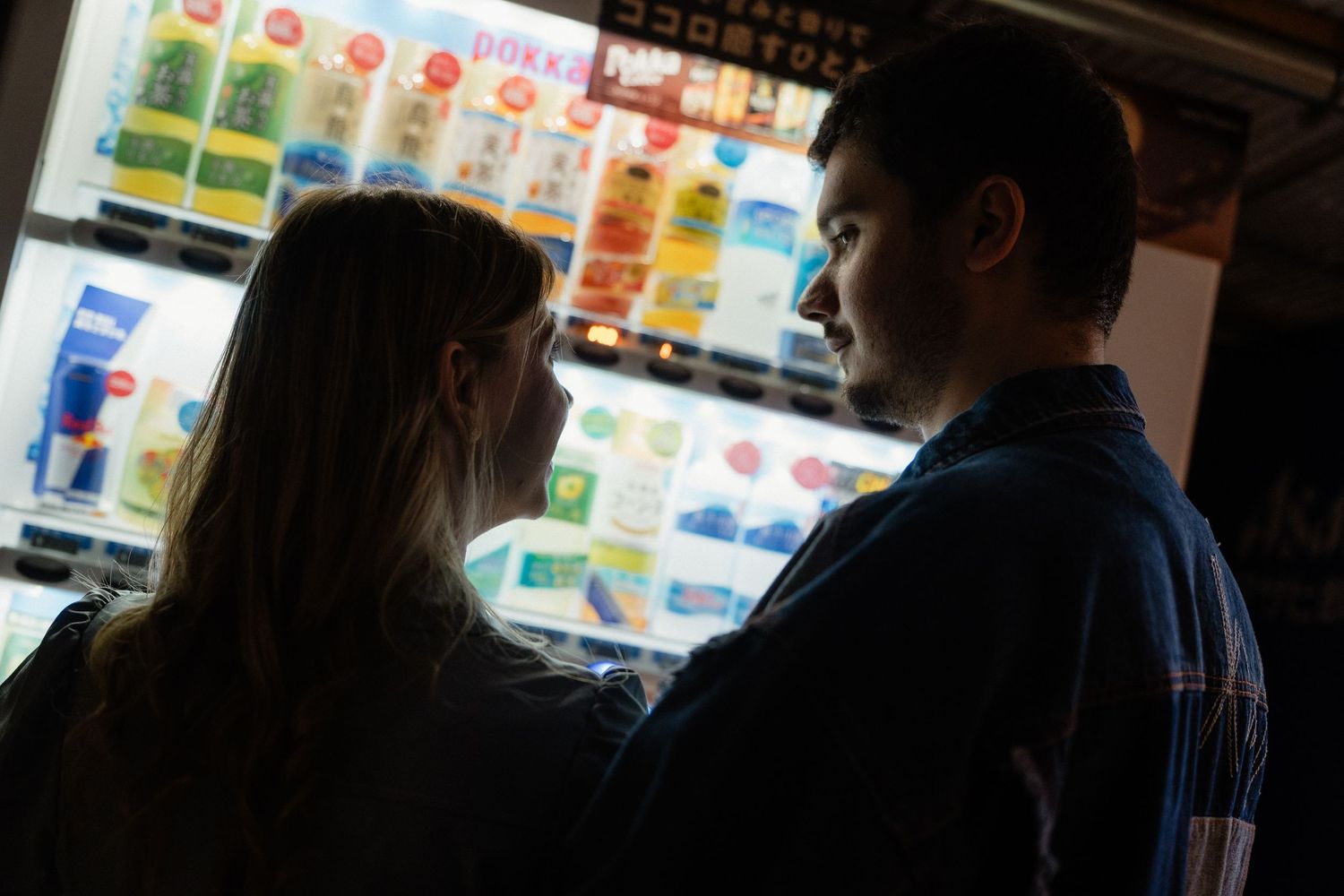 Couple silhouetted against colorful Japanese vending machines at night.