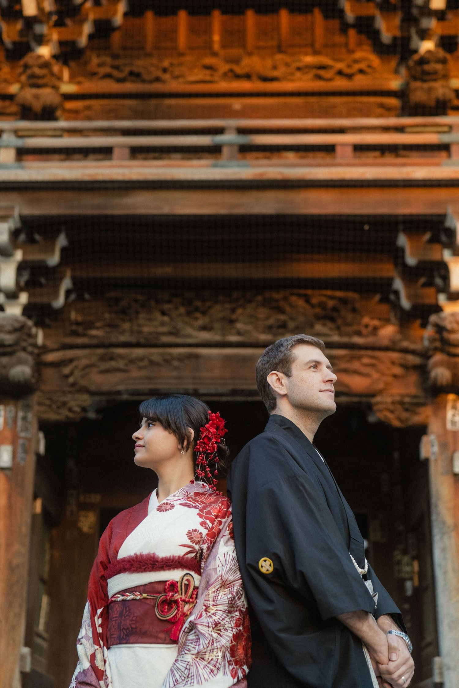 Couple in traditional Japanese kimono and hakama posing back-to-back at an ornate wooden temple.