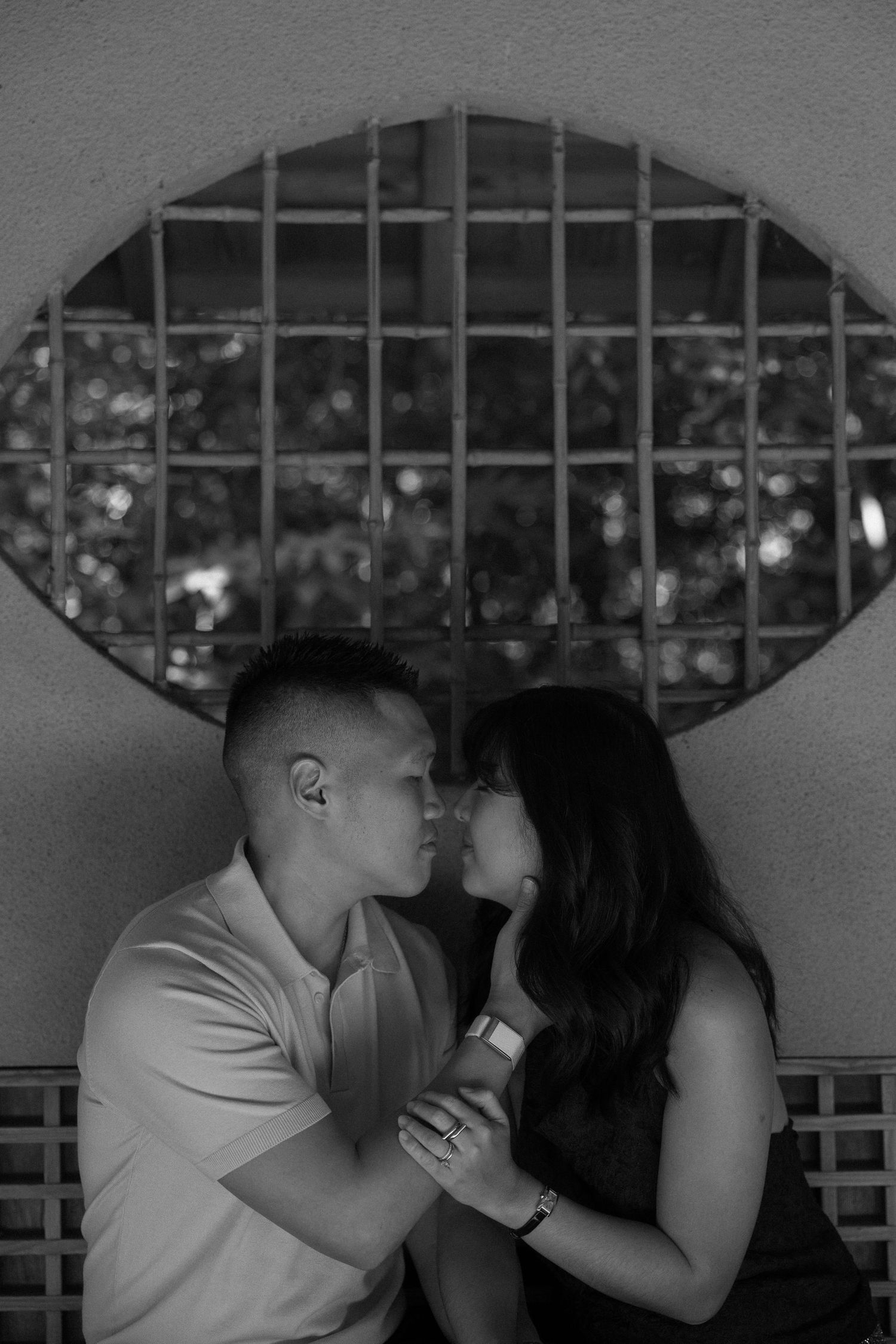 Black and white photo of a romantic couple sharing an intimate moment in front of an oval window.
