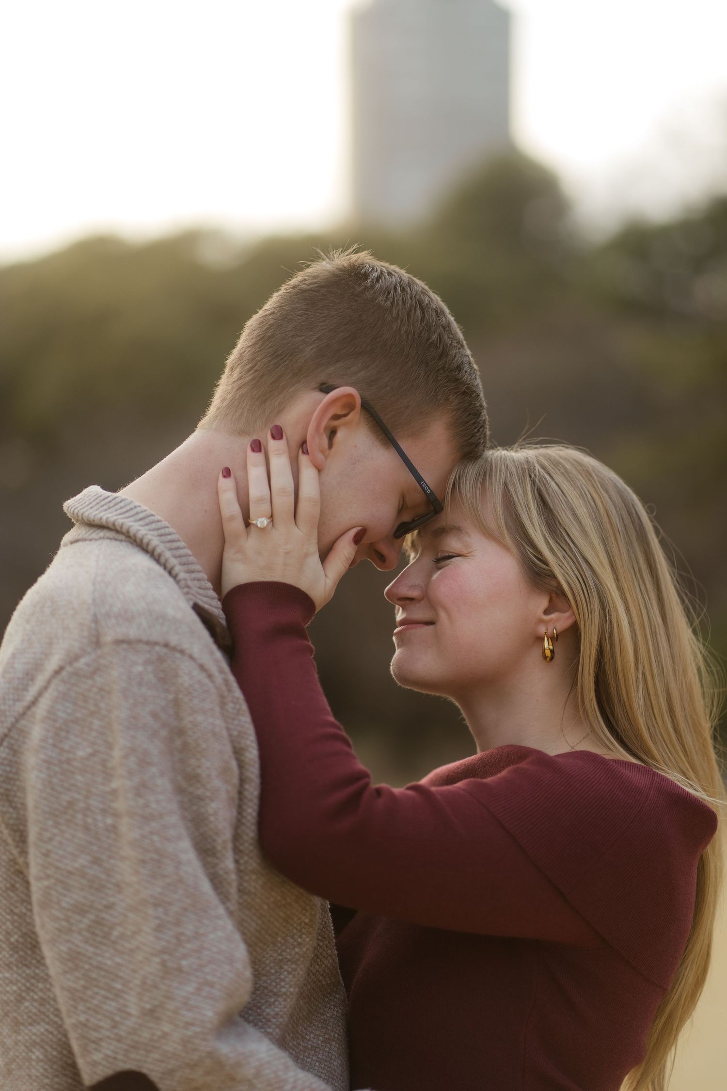 Romantic couple sharing a tender moment outdoors at golden hour, woman smiling as she gently holds mans face.