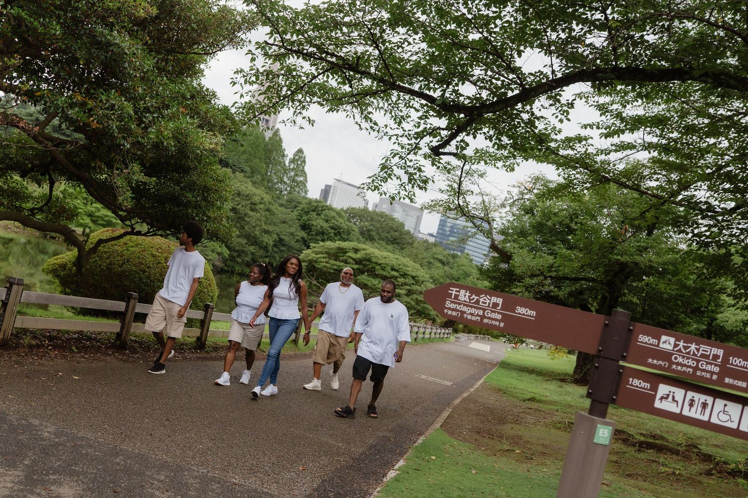 Group of young people walking on a path in a lush green Japanese park with city buildings visible.