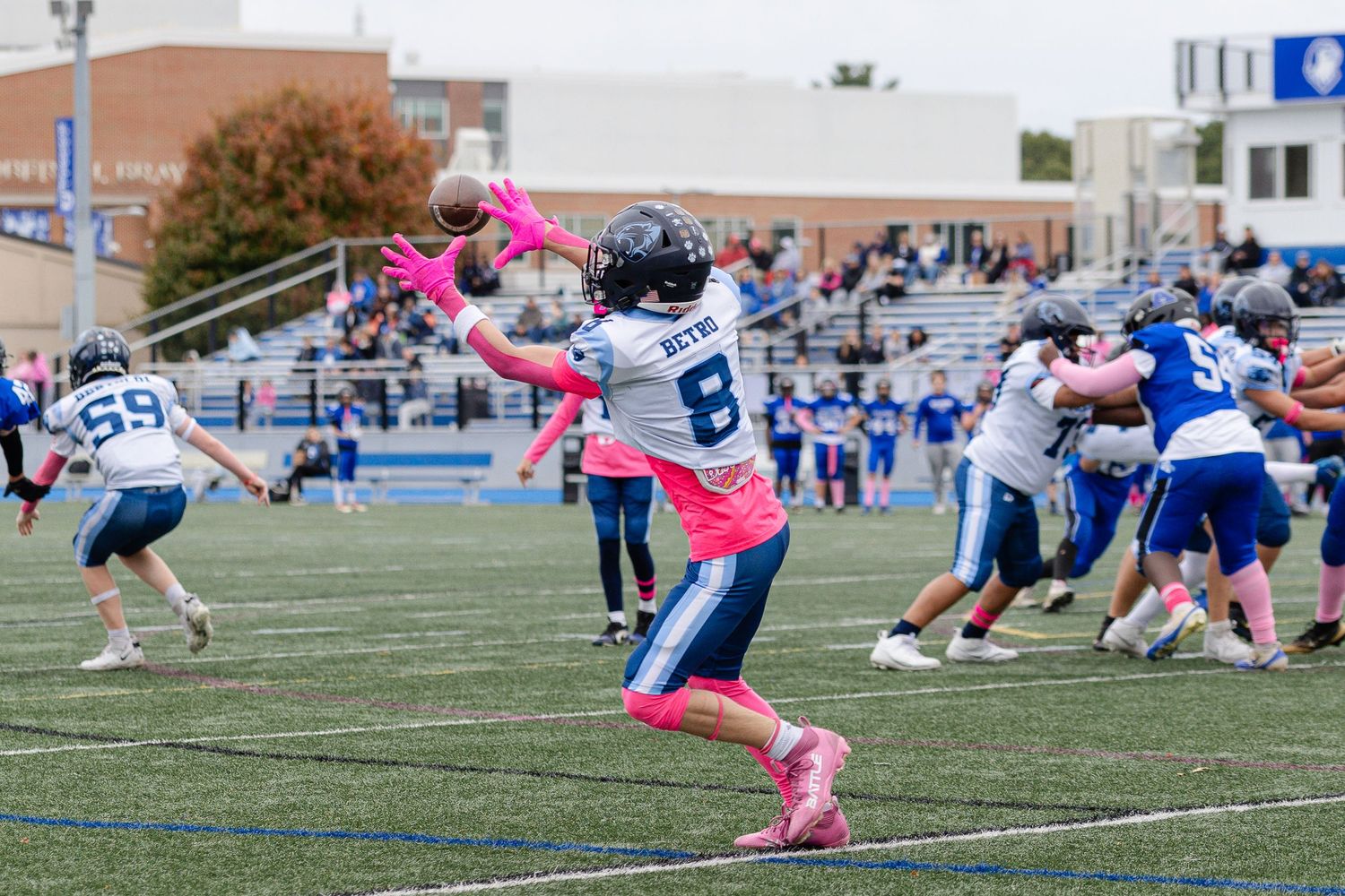 Football player in pink gloves catches a pass during a youth tackle football game on a blue turf field.