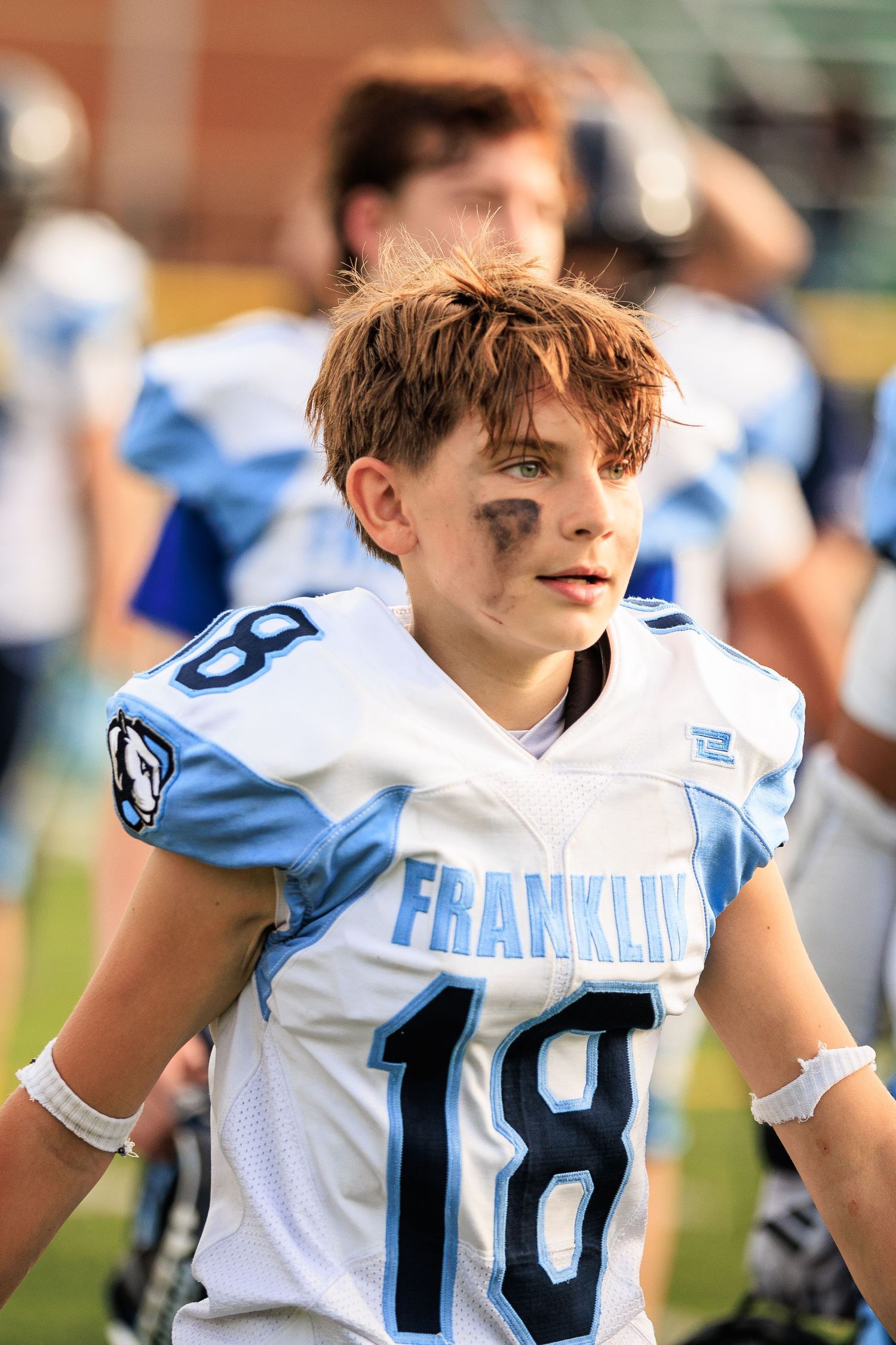 Young football player wearing Franklin jersey number 18 stands on the sideline with eye black on his cheeks.