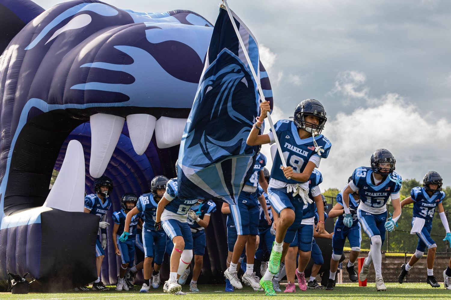 Football team running through inflatable tunnel onto field before game day.