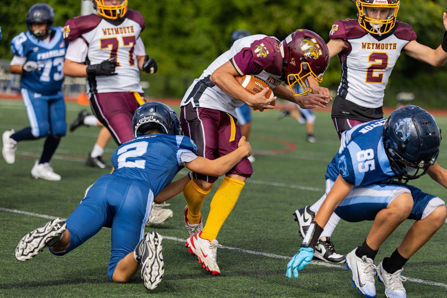 Youth football players tackling opponent during competitive game on green field.