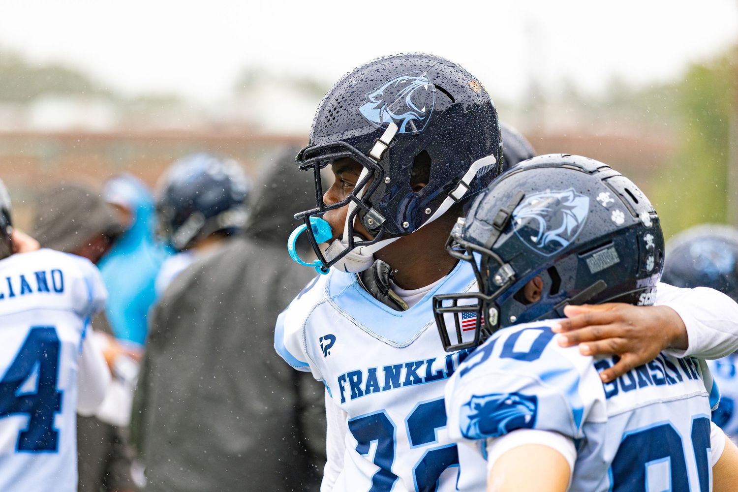 Two youth football players in Franklin jerseys share a celebratory hug on the field during a game.