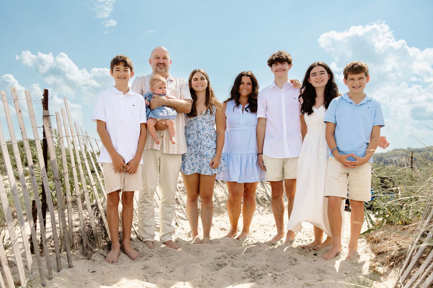 Happy family of eight posing together on a sunny beach with sand dunes.