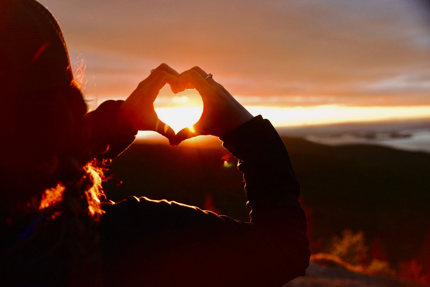 Silhouette of person forming heart shape with hands against stunning golden sunset sky.