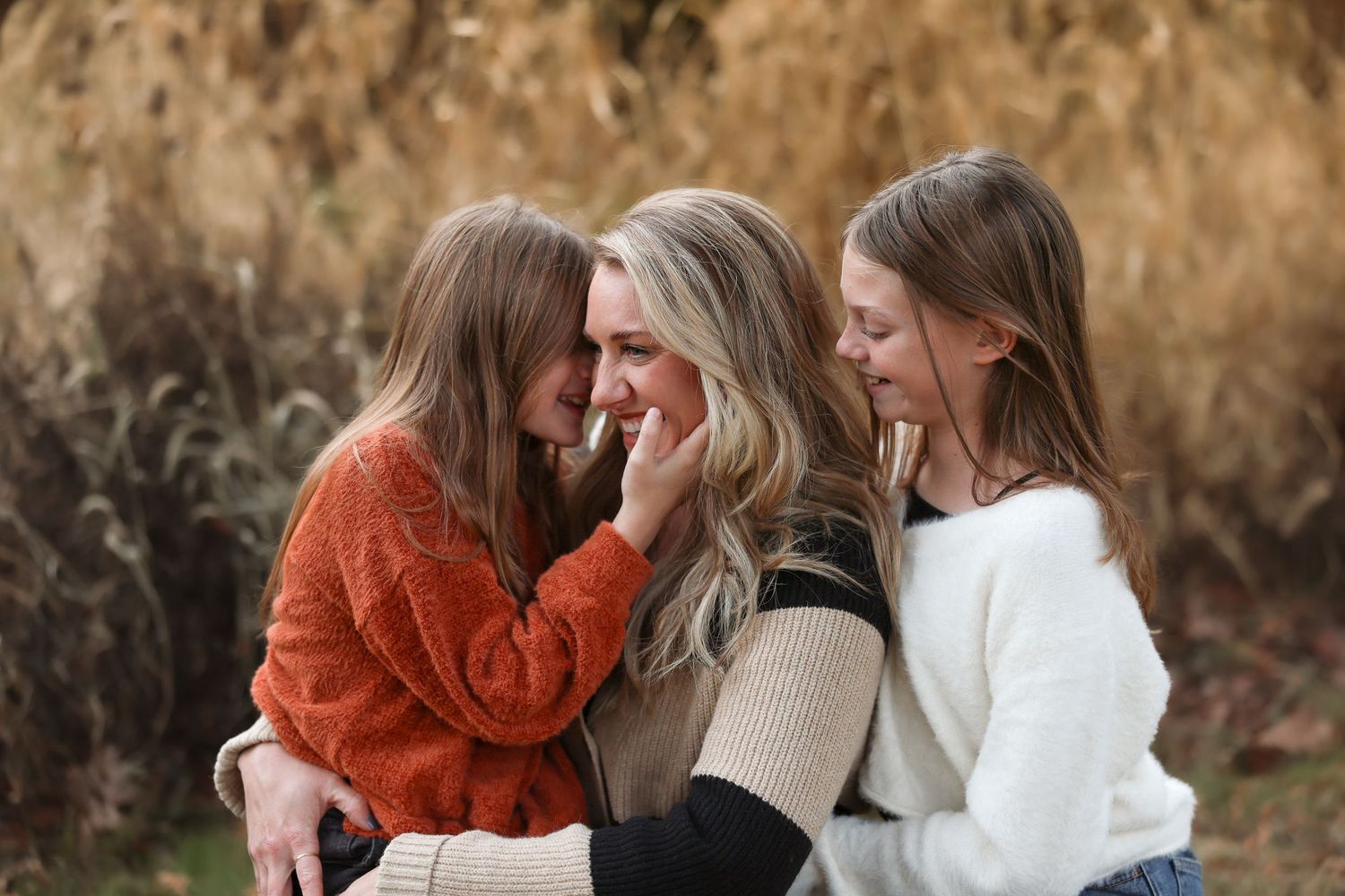 Mother laughing with two daughters in warm autumn outdoor portrait session.