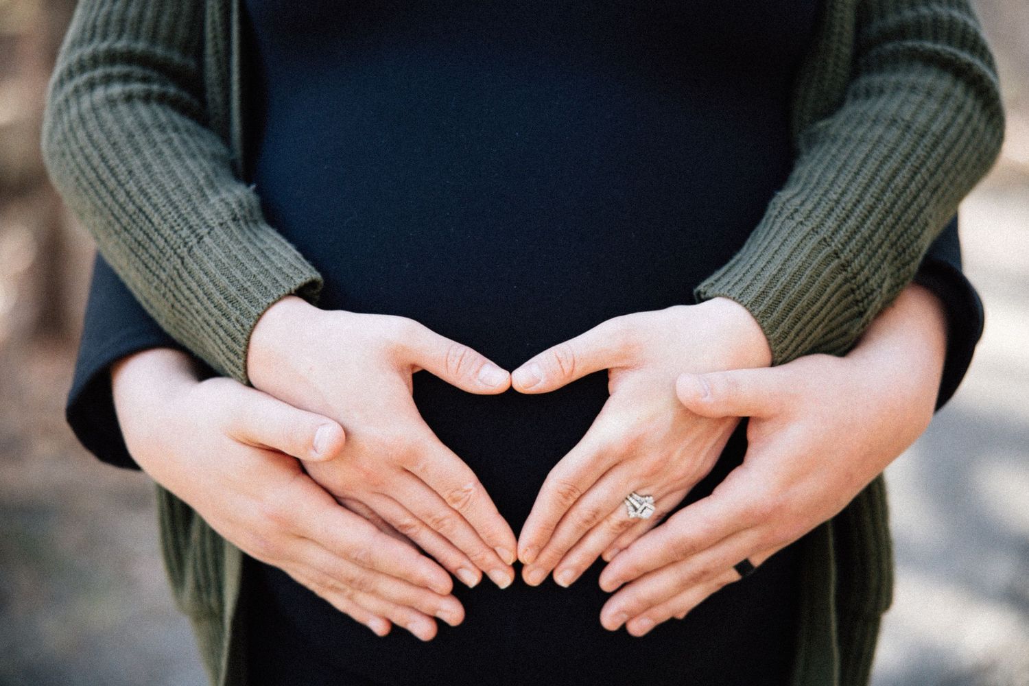 Two pairs of hands form a heart shape over a pregnant belly during a maternity photo.
