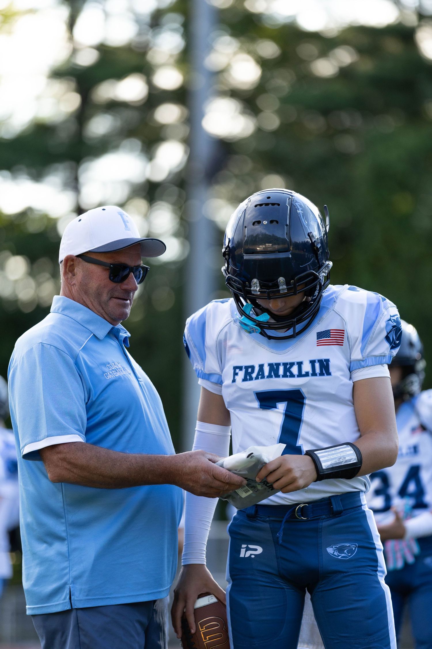 Football coach reviewing play card with Franklin jersey number 7 player on sideline.