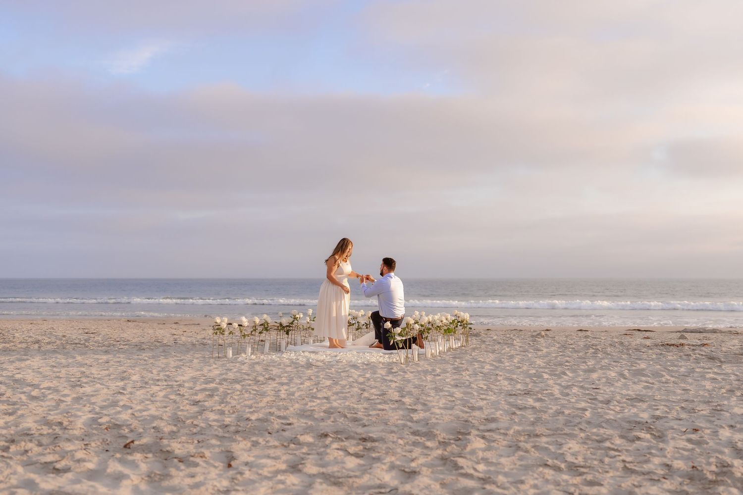 Man proposing on one knee to woman on beach at sunset with floral arrangement. Coronado beach