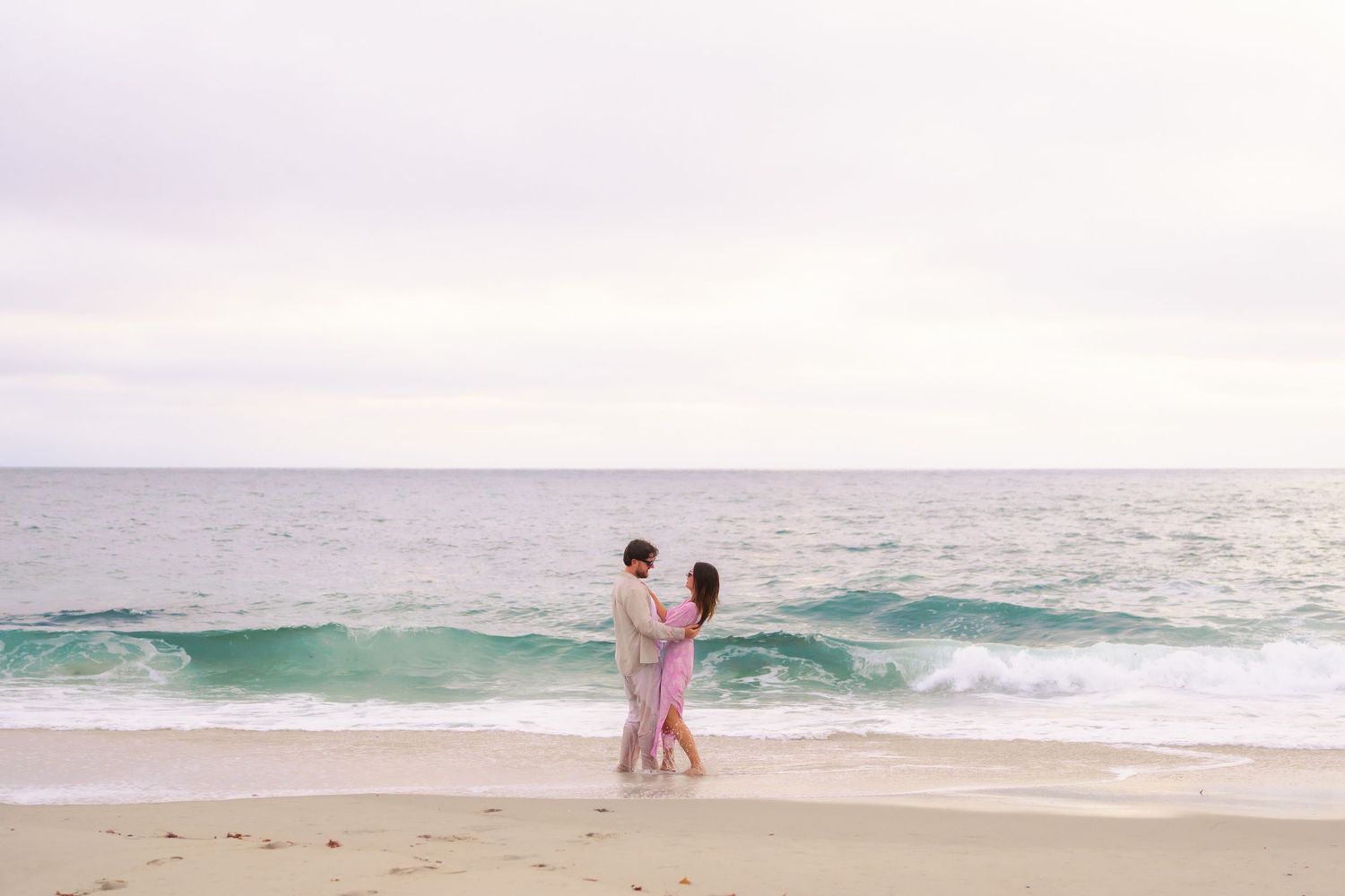 Couple dancing together on sandy beach with ocean waves in the background.