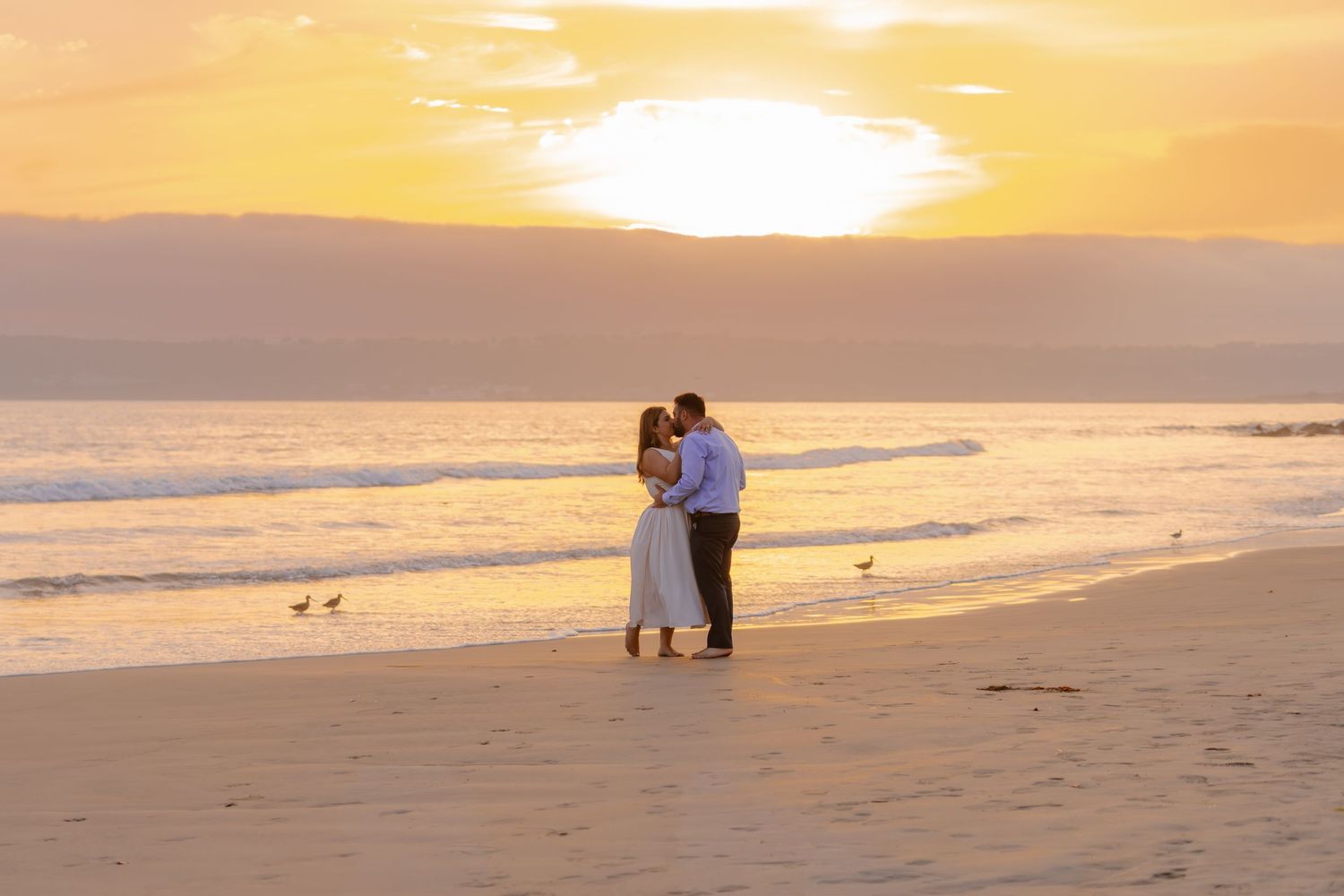 Romantic couple kissing on beach at golden sunset with ocean waves behind them. Coronado beach
