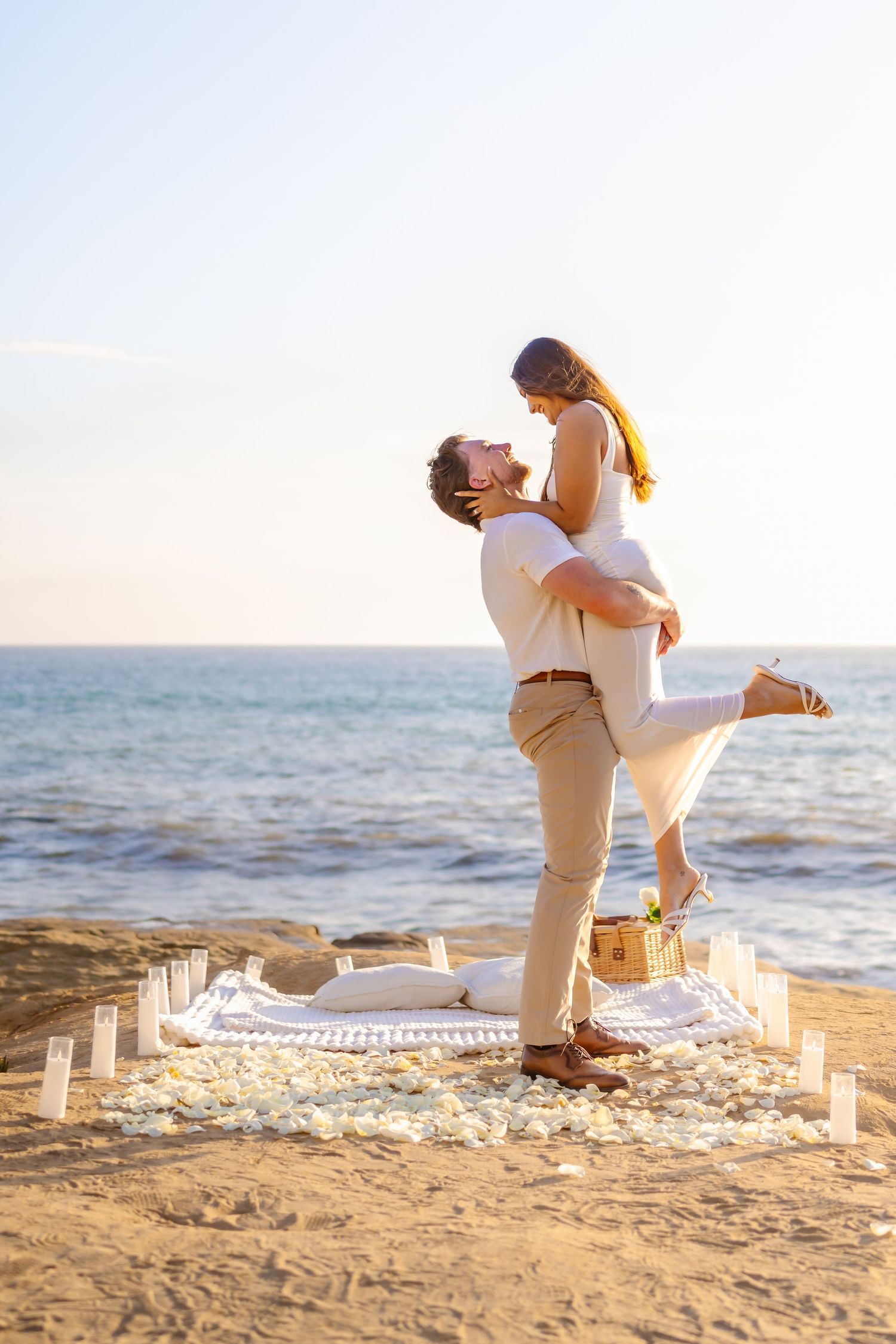 Man lifting woman joyfully at beach picnic setup with candles and rose petals Santa Cruz Cliffs