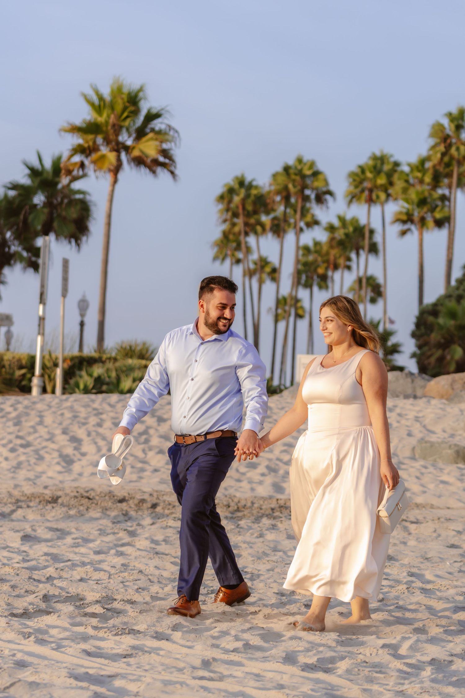 Happy couple holding hands walking on sandy beach with palm trees in background. Coronado beach