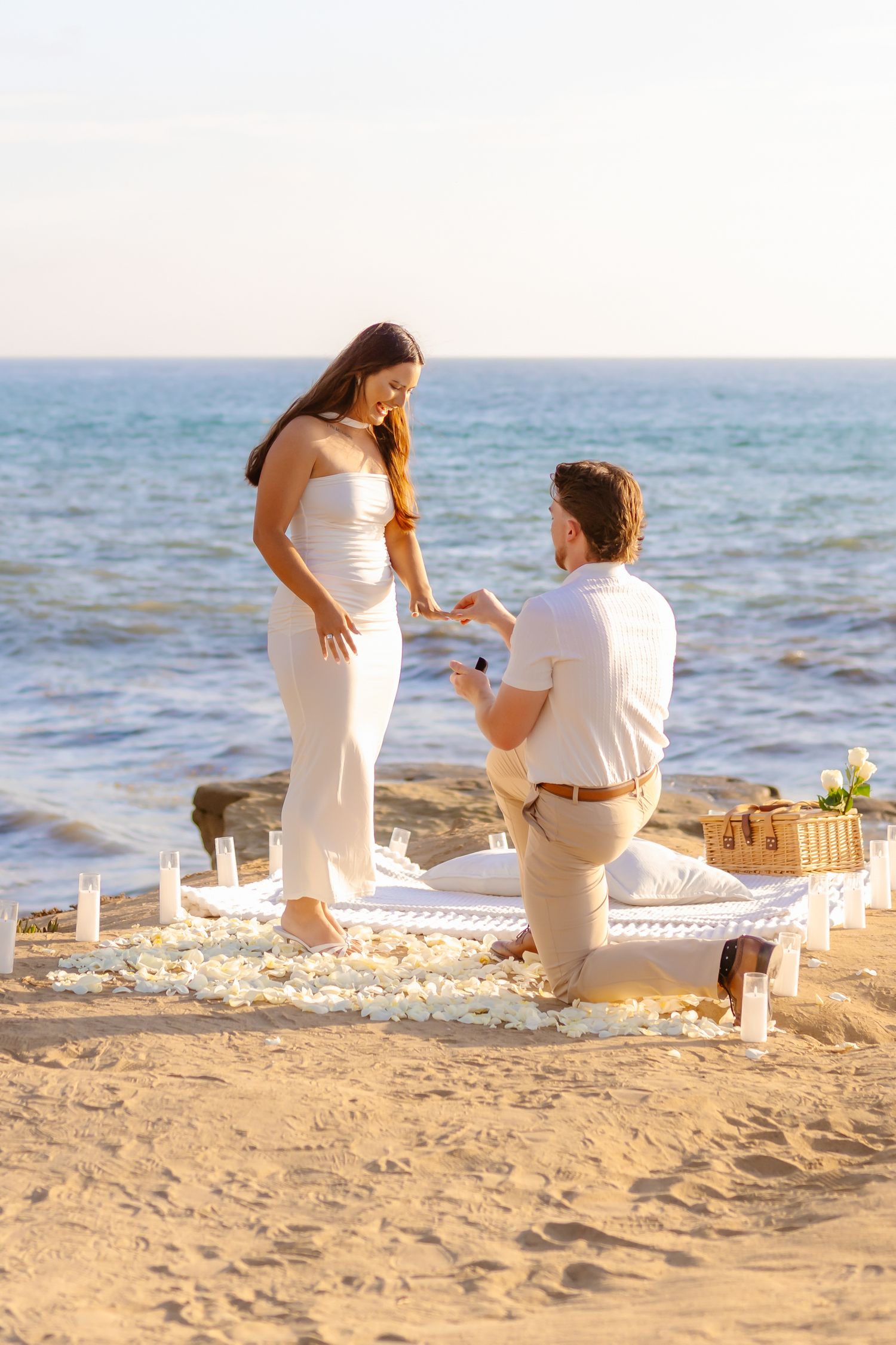 Man proposing on one knee to woman at candlelit beach picnic at sunset Santa Cruz Cliffs
