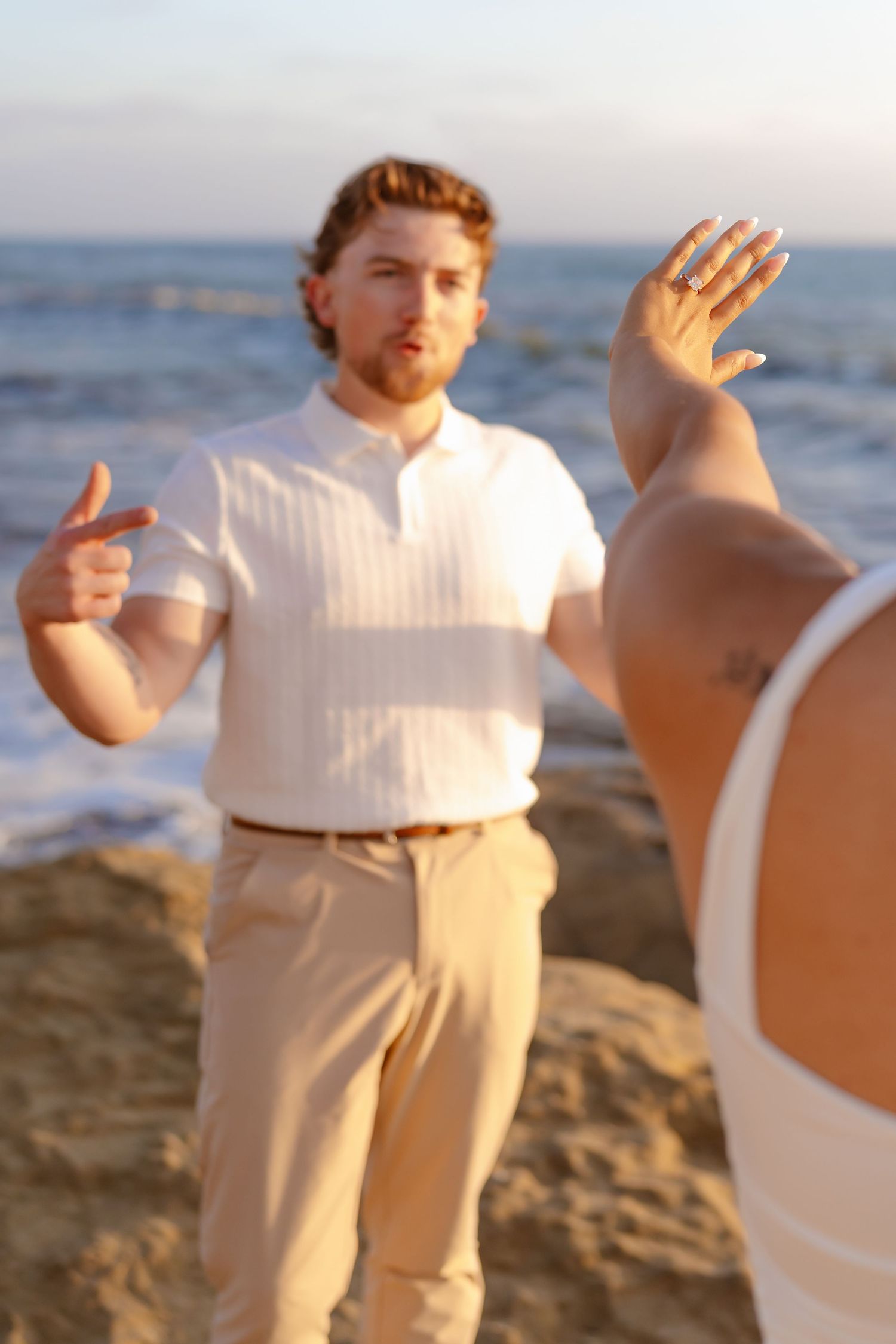Man in white shirt gesturing at beach during golden hour sunset photography session.