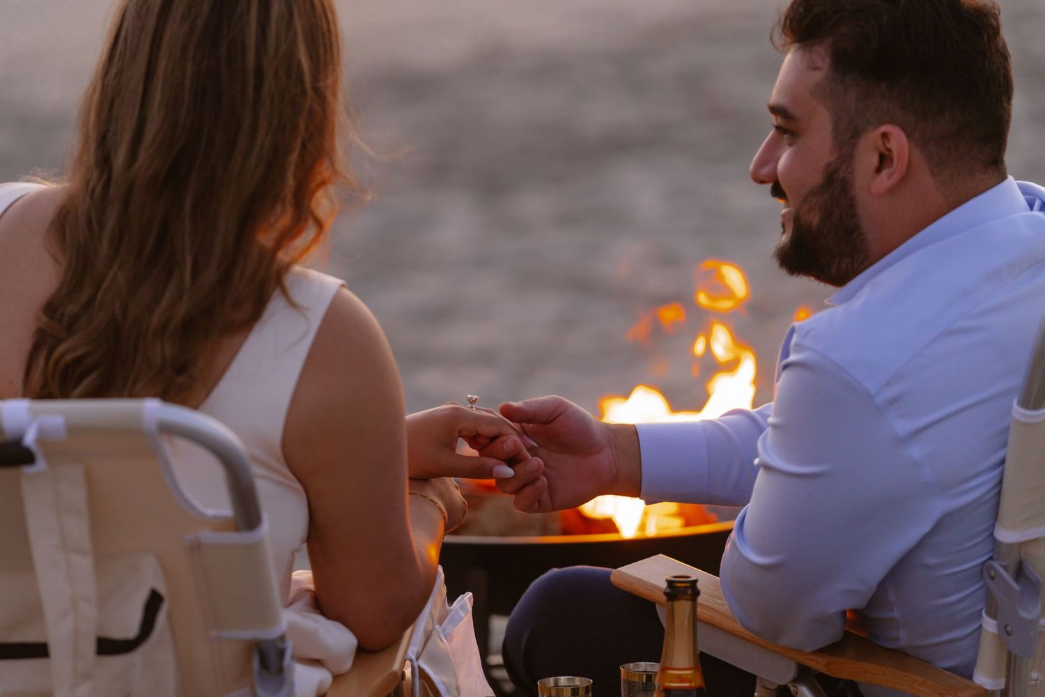 Man placing engagement ring on womans finger during candlelit beach proposal at night. Coronado beach